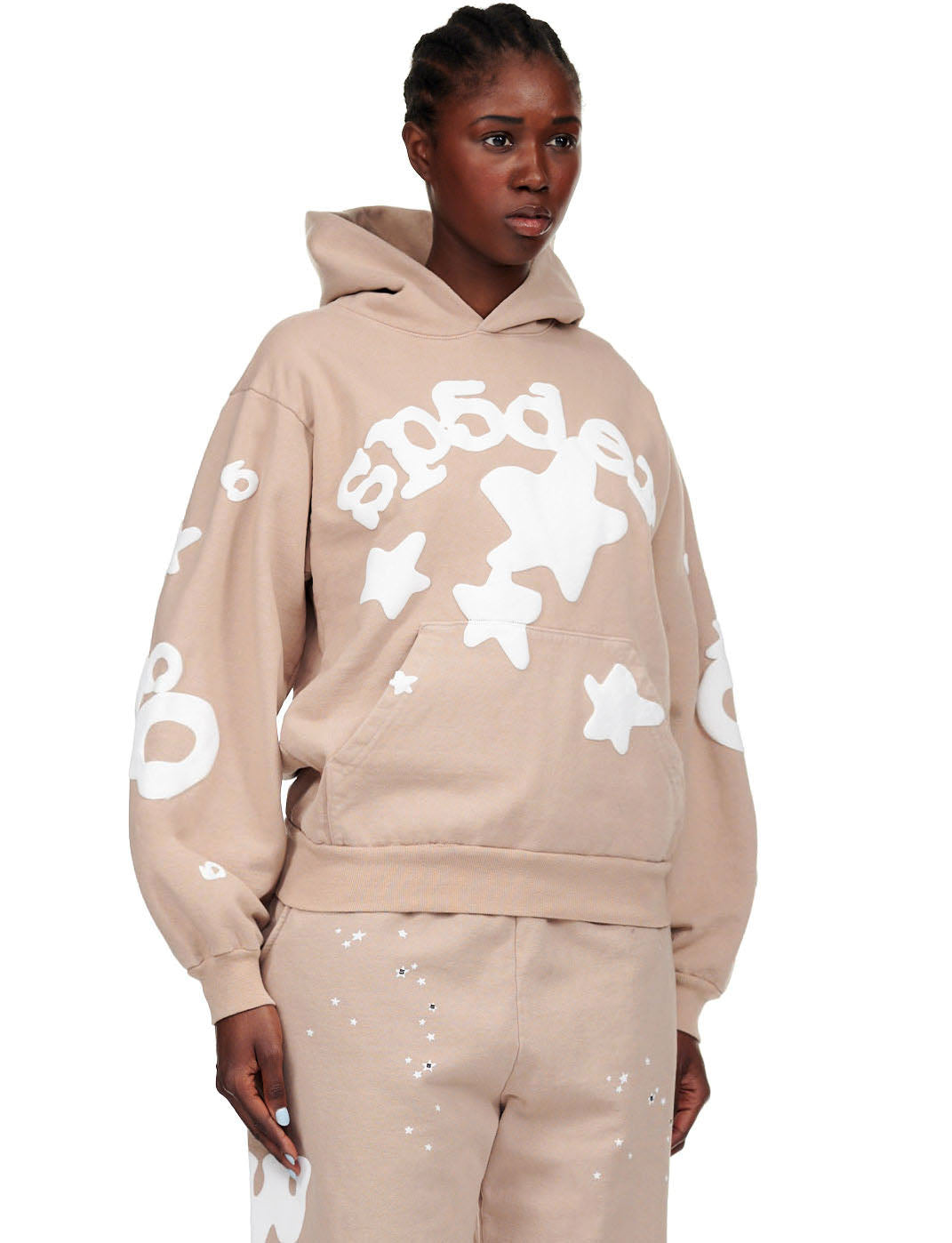 Female model in a sand beluga hoodie with white puff print SP5DER text and stars.
