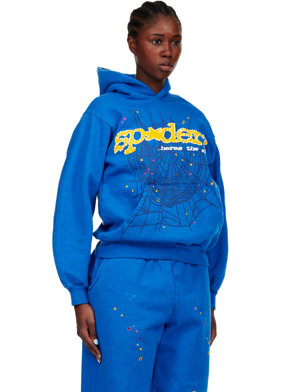 Female model in a blue TC BLUE HOODIE with yellow SP5DER! text, web, and star prints.