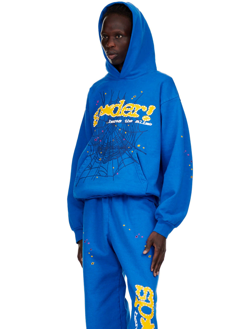 Male model in a blue fleece hoodie with yellow "SP5DER!" text, a spider web, and star prints.