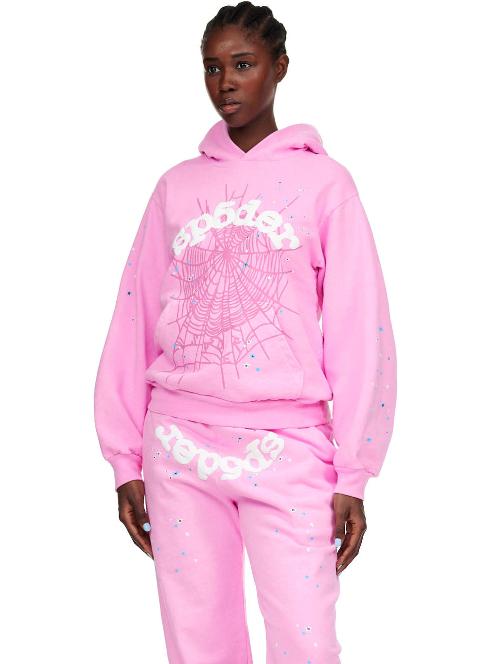 Female model in a pink fleece hoodie and sweatpants with white puff print spiderweb and "sp5der" text.