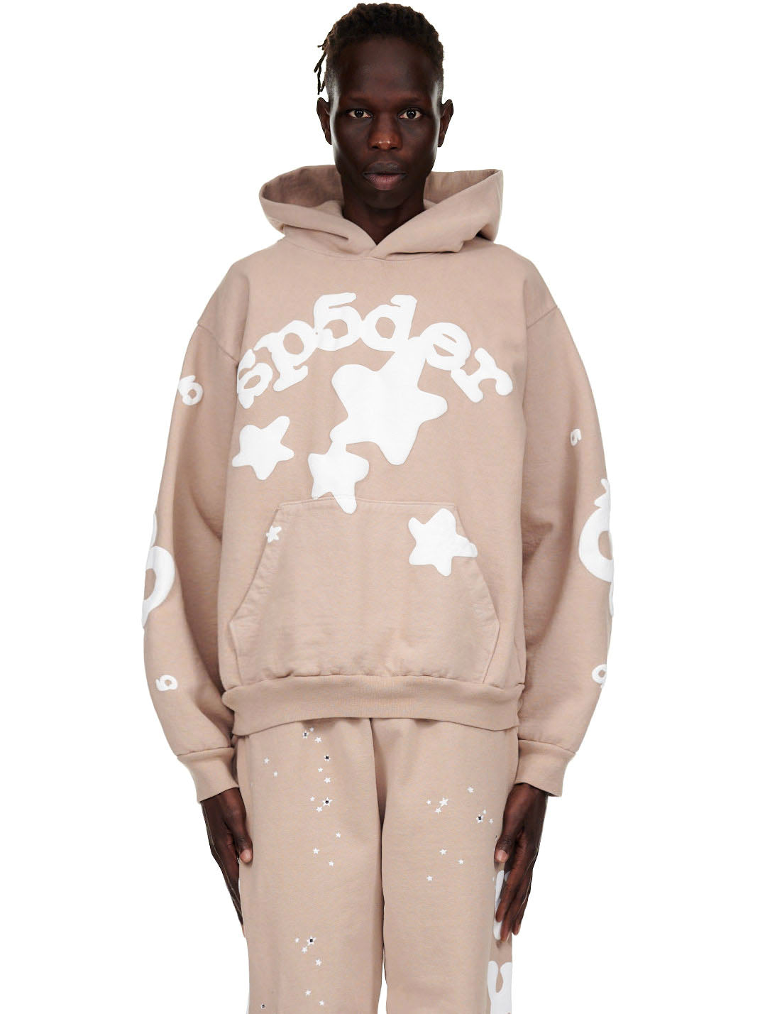Male model in a sand Beluga hoodie with white puff print "sp5der" text and stars, matching sweatpants.