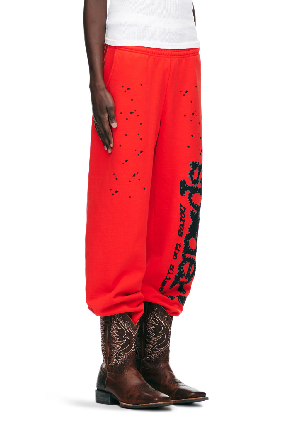 Red 23oz fleece sweatpants with black SP5DER motif, star prints, and "P*NK" text, paired with cowboy boots.