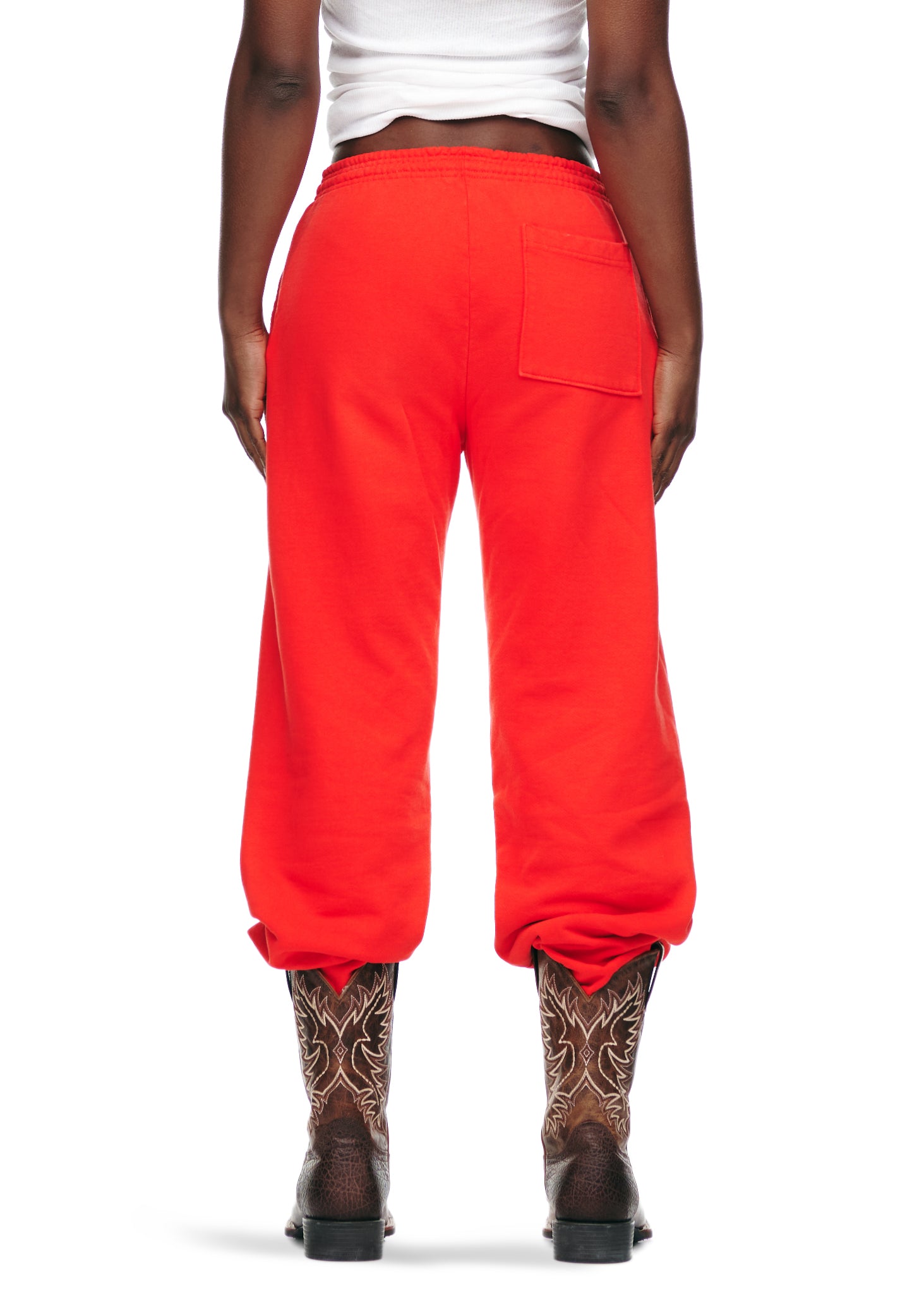 Rear view of a person wearing bright red P*NK V2 fleece sweatpants with a back pocket and cowboy boots.