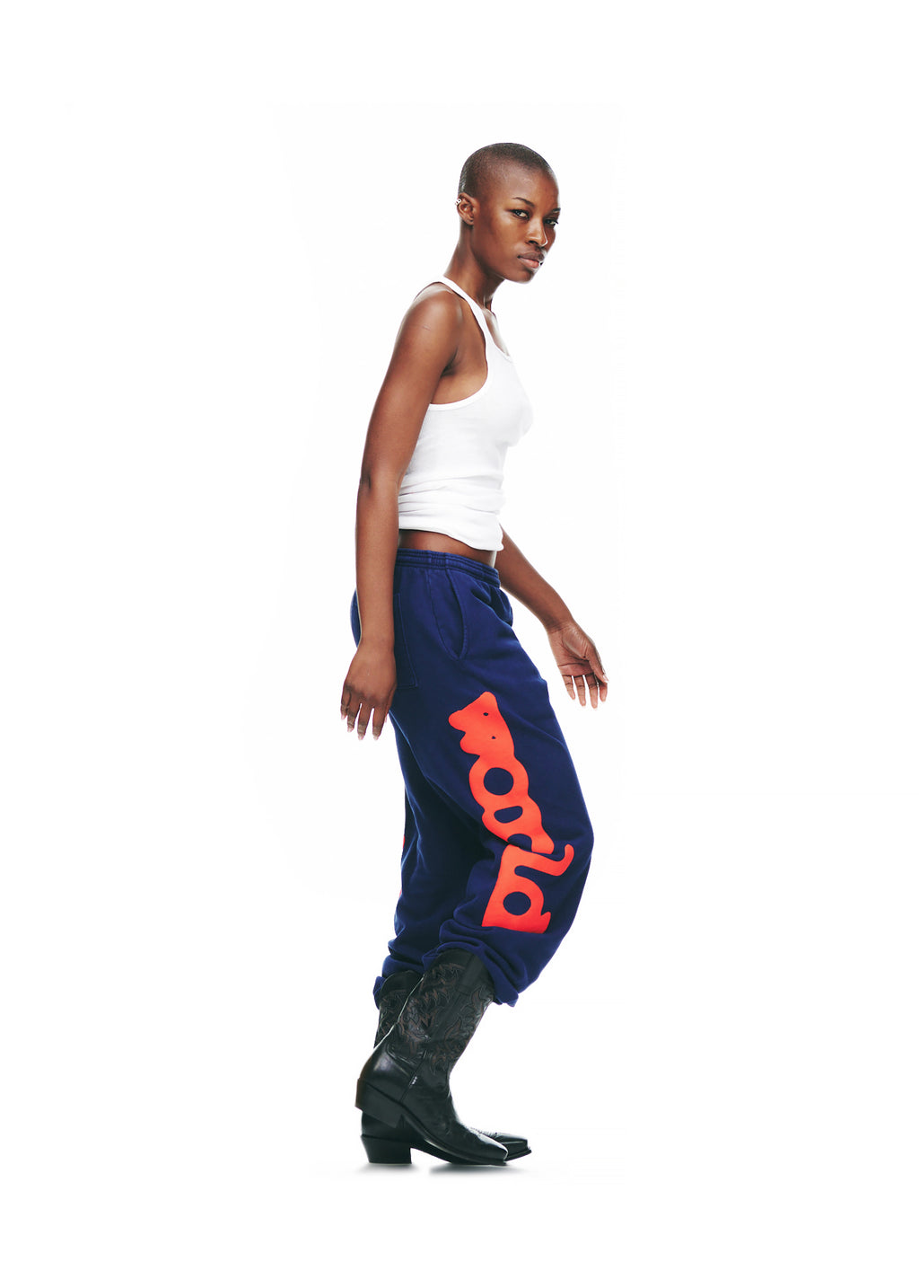 Model wearing navy BELUGA SWEATPANTS with red "Worldwide" puff/discharge print down the legs, paired with a white tank top and black cowboy boots.