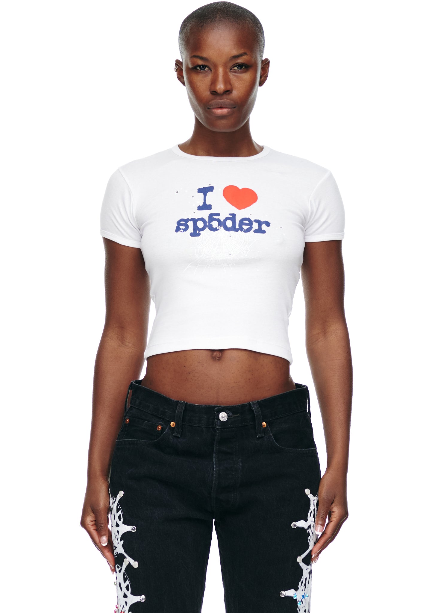 Female model in white cropped cotton "I heart sp5der" graphic tee and black jeans.