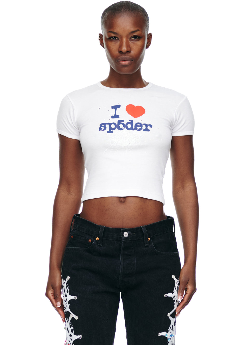 Female model in white cropped cotton "I heart sp5der" graphic tee and black jeans.