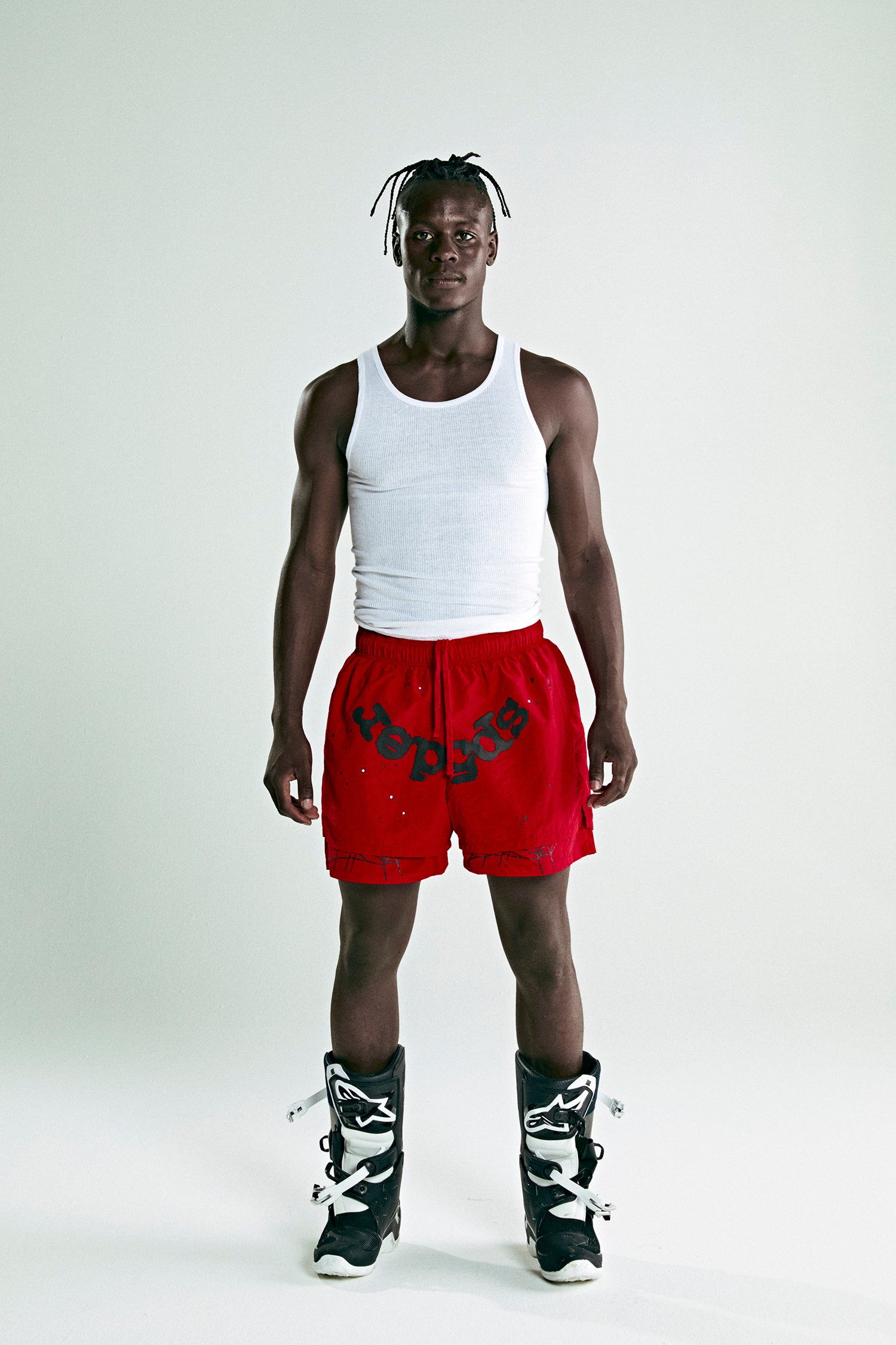 Man in red OG WEB Double Layer Shorts with "SP5DER" text, white tank top, and black boots.