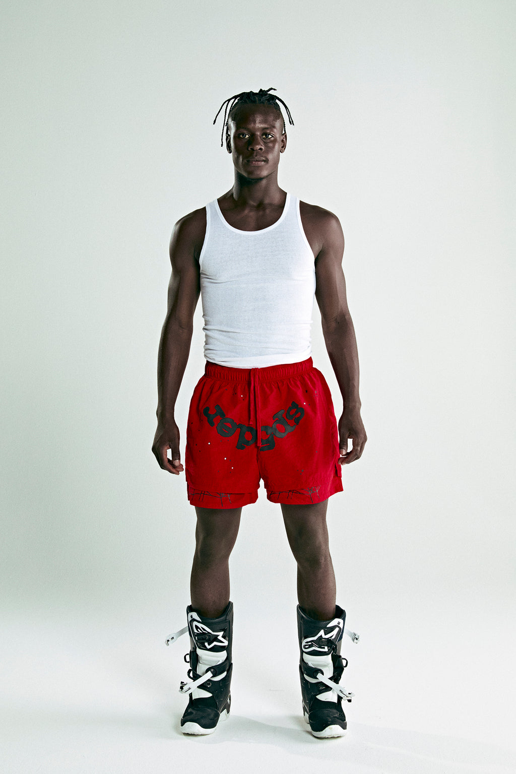 Man in red OG WEB Double Layer Shorts with "SP5DER" text, white tank top, and black boots.