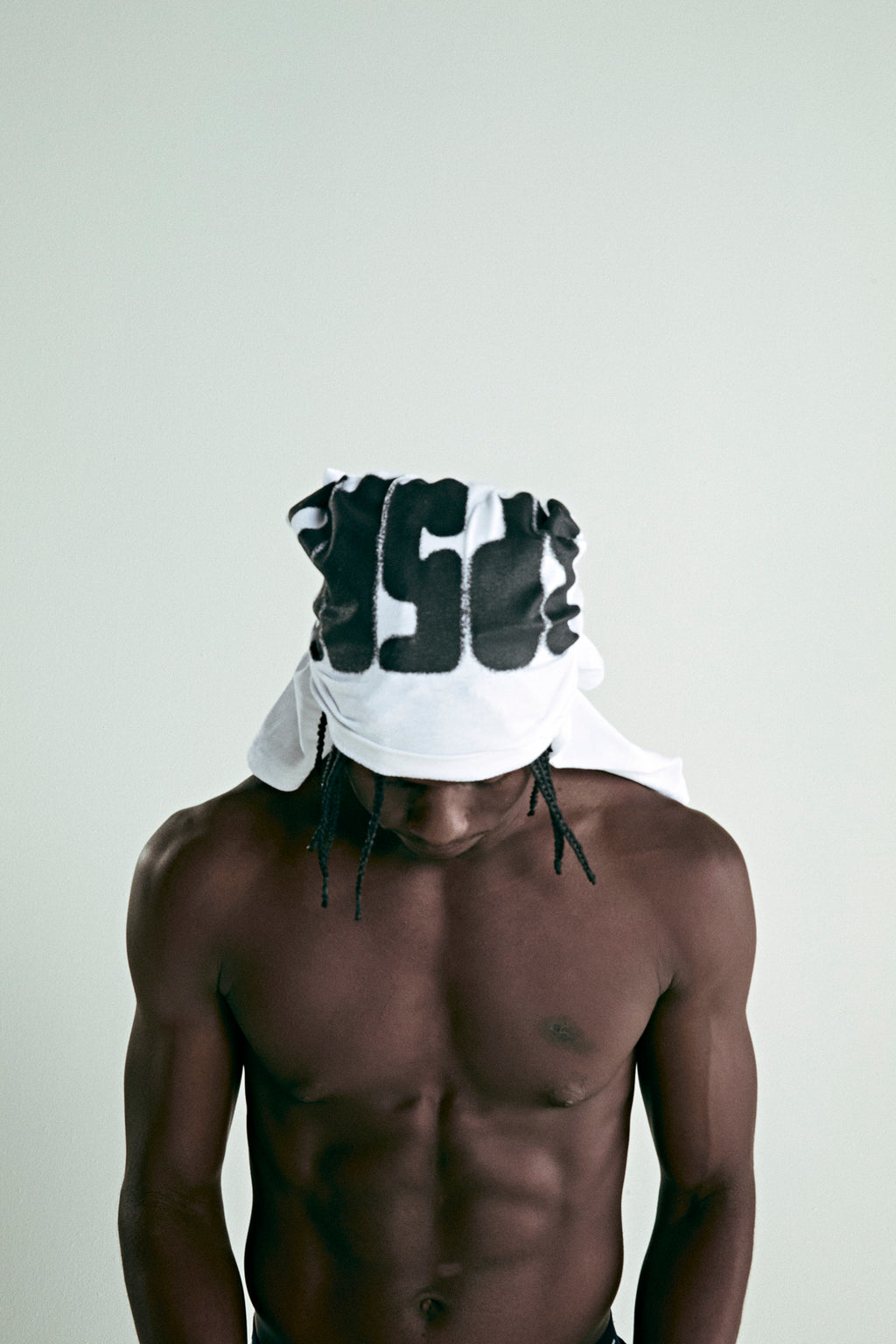 Man wearing a white cotton tee with a black 'SP5DER' text print on the front, styled as a headwrap.