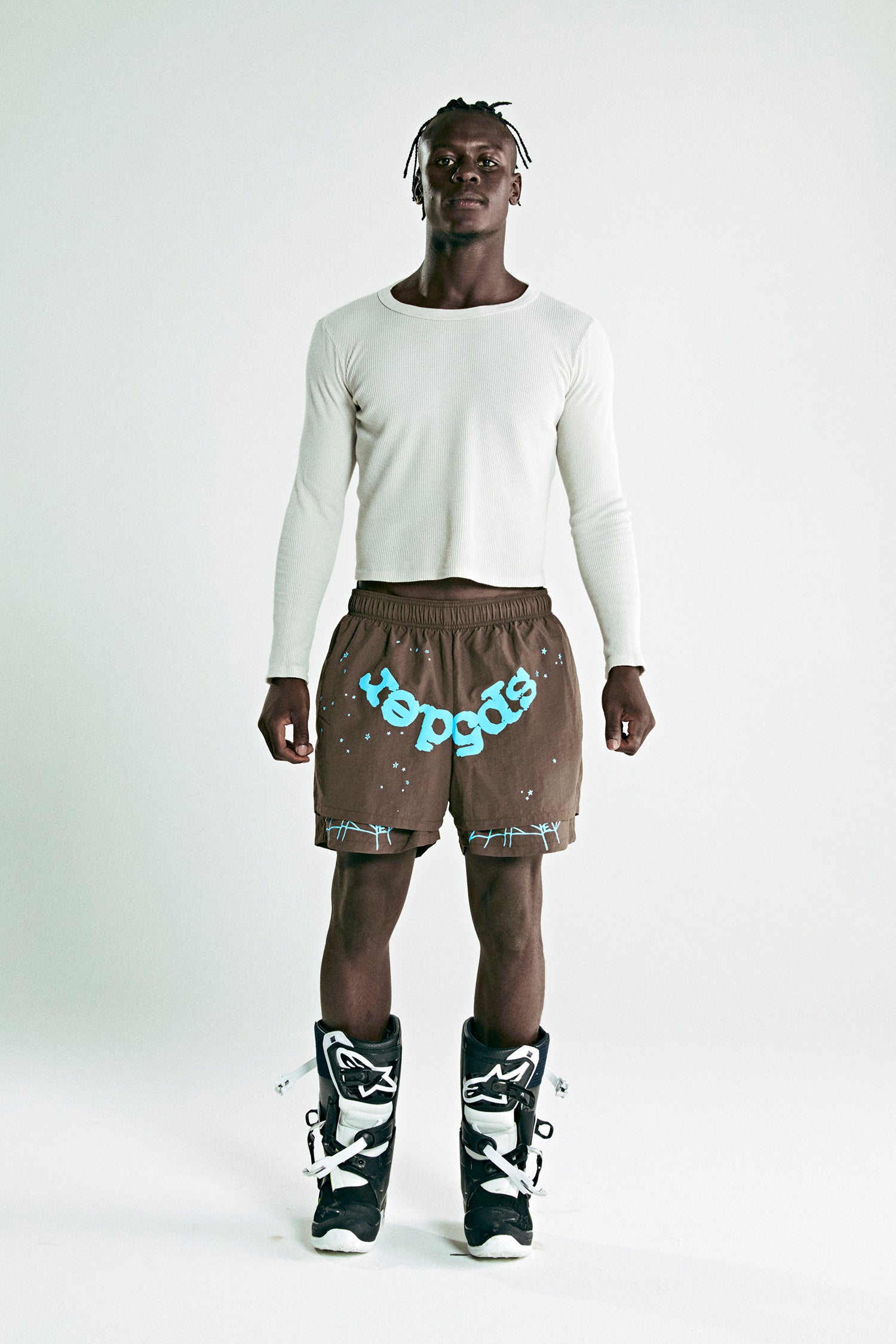 Brown OG WEB DOUBLE LAYER SHORT with blue "sp5der" text and star print, worn by a model.