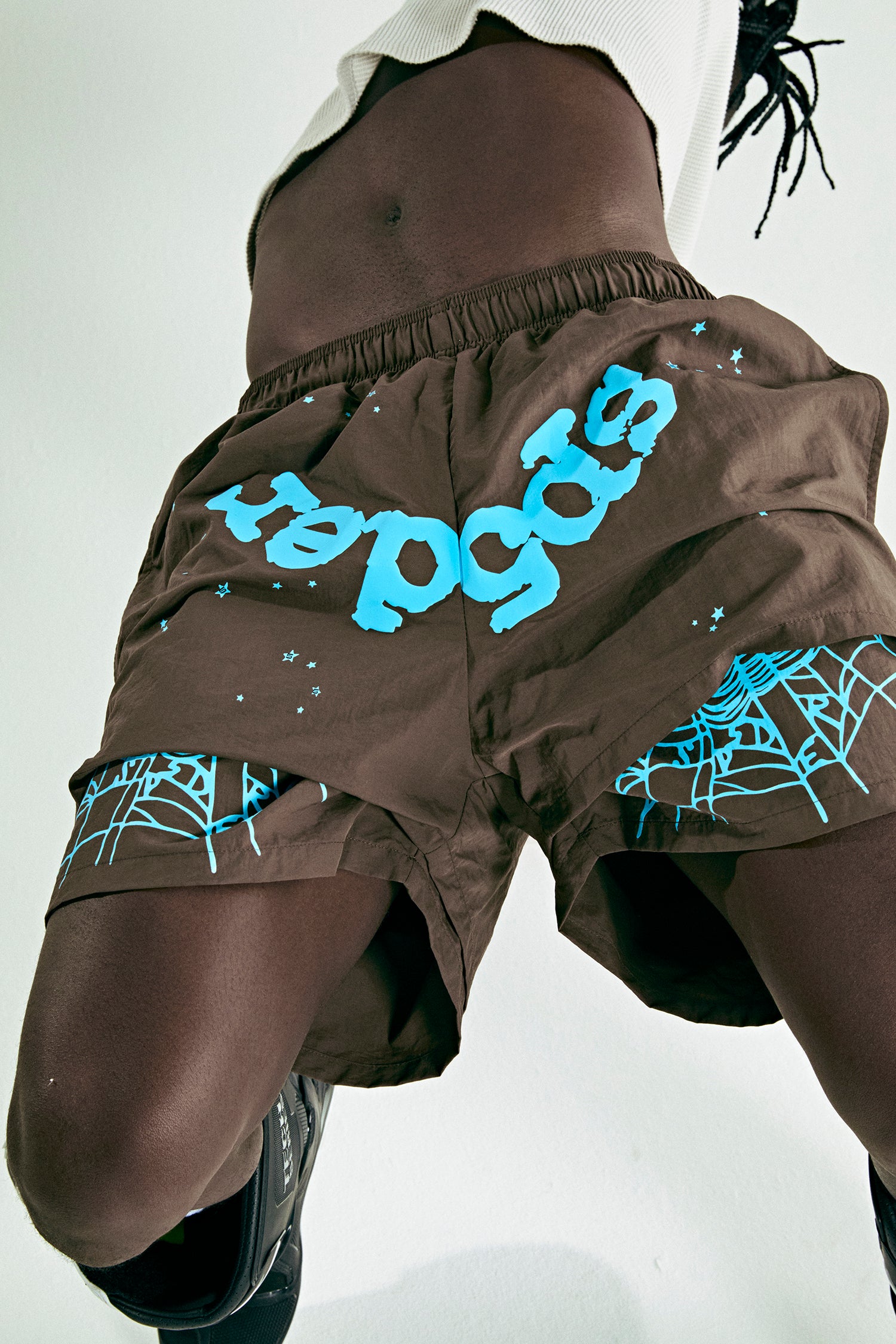 Brown nylon OG WEB Double Layer Shorts with blue "OG SP5DER" text, stars, and spiderweb print.