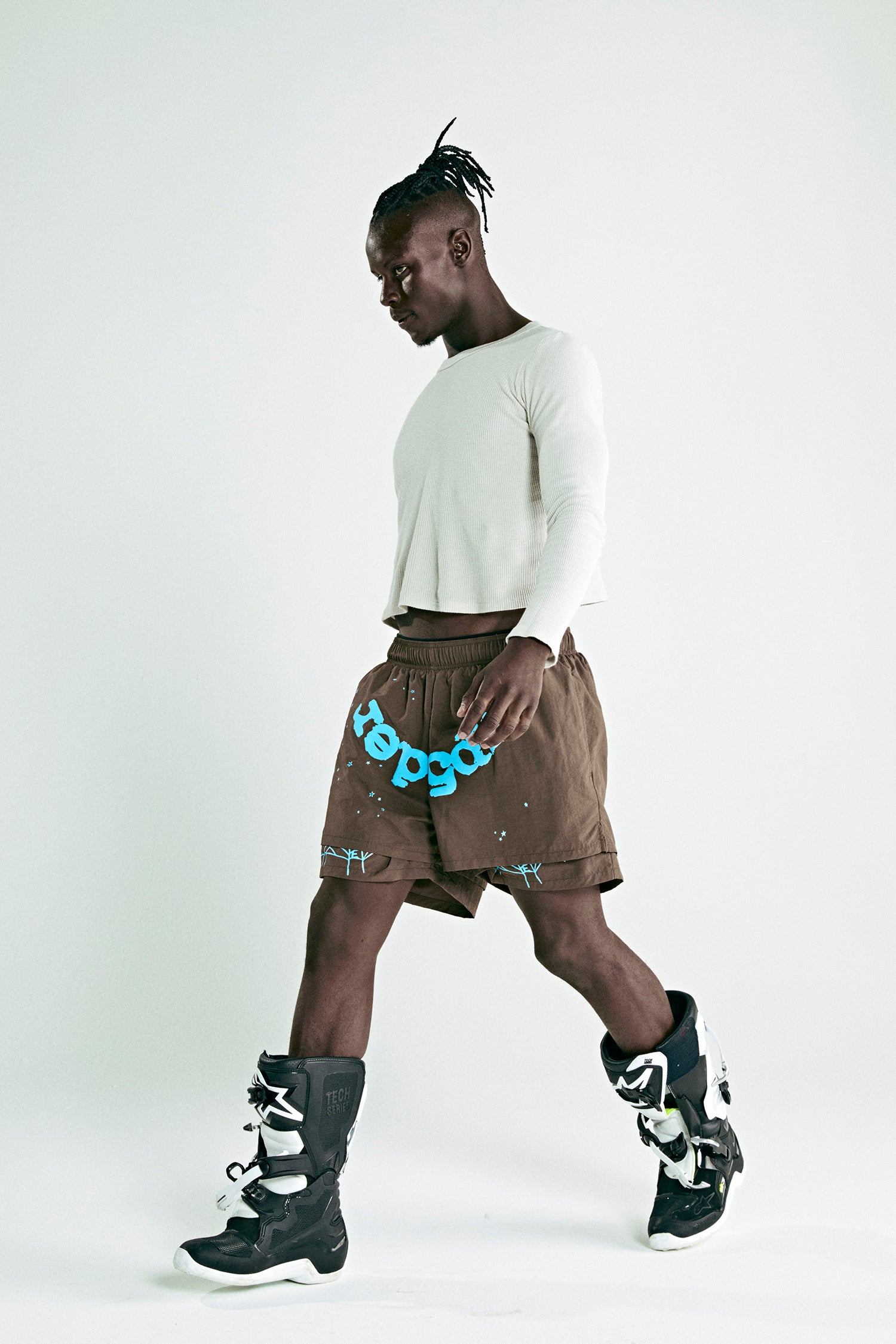 Brown OG WEB DOUBLE LAYER SHORT with blue "sp5der" text, white top, and black boots.