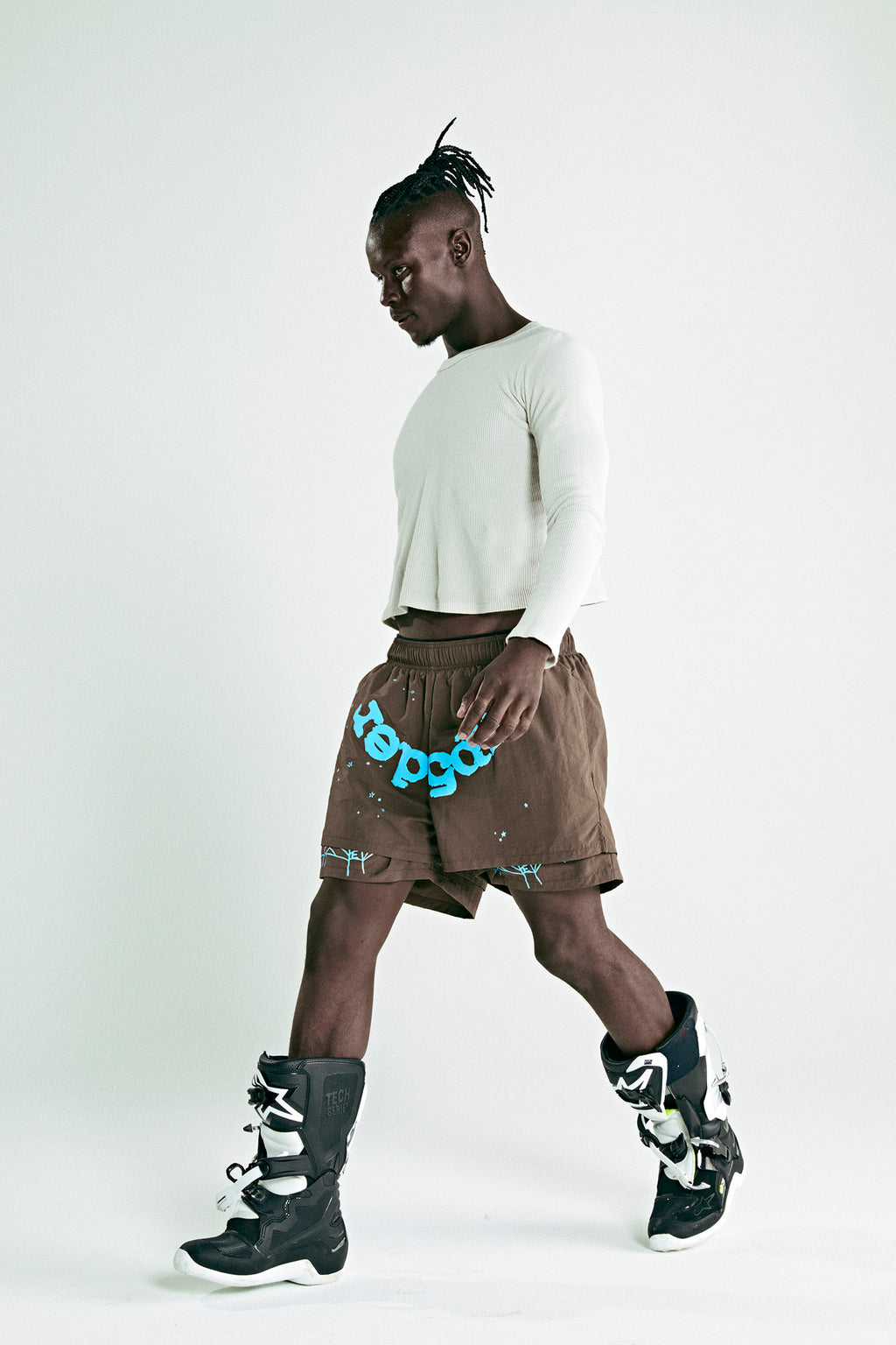 Brown OG WEB DOUBLE LAYER SHORT with blue "sp5der" text, white top, and black boots.