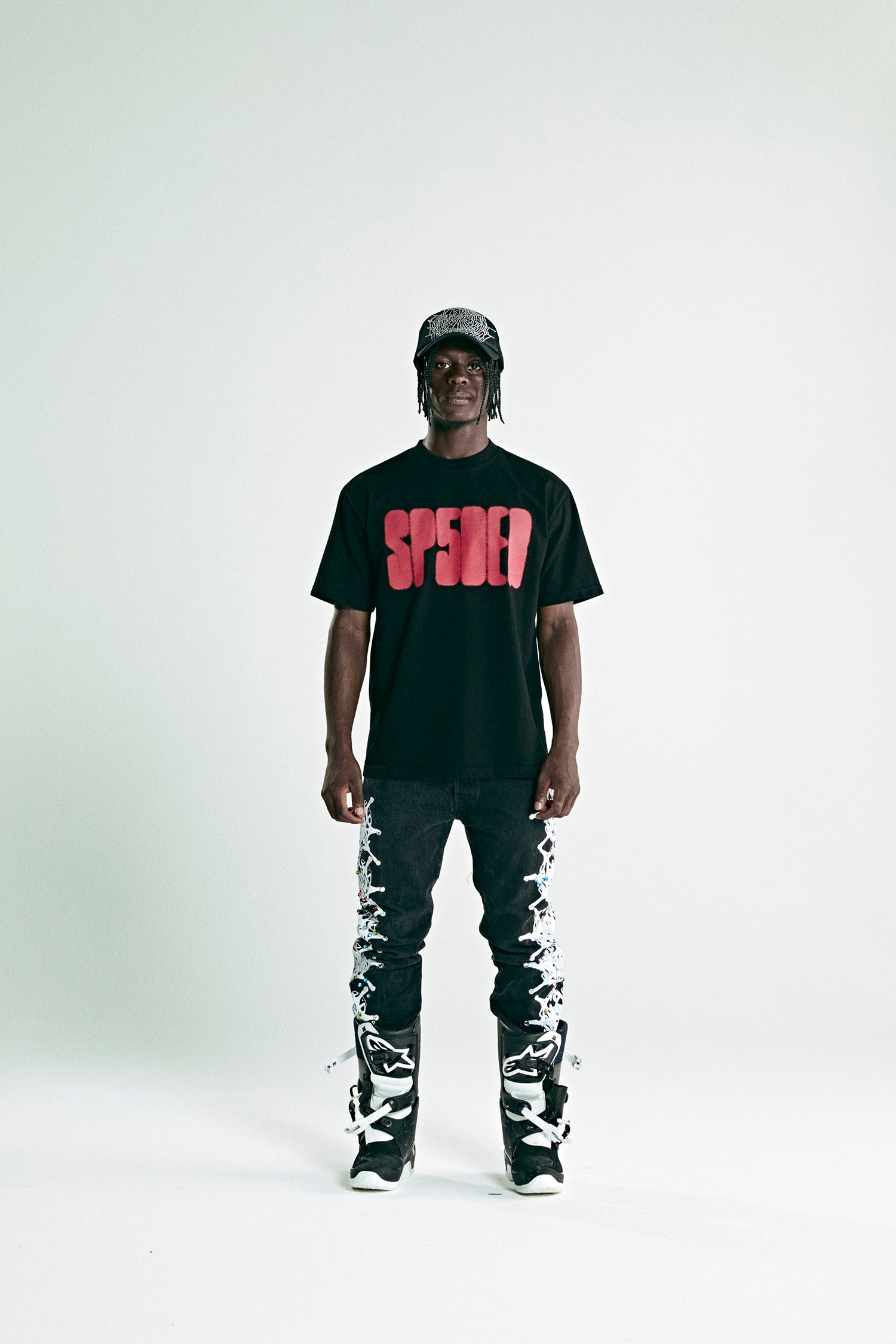 Black cotton FOCUSED LOGO TEE with red 'SP5DER' text print, worn by a man with black jeans and a cap.
