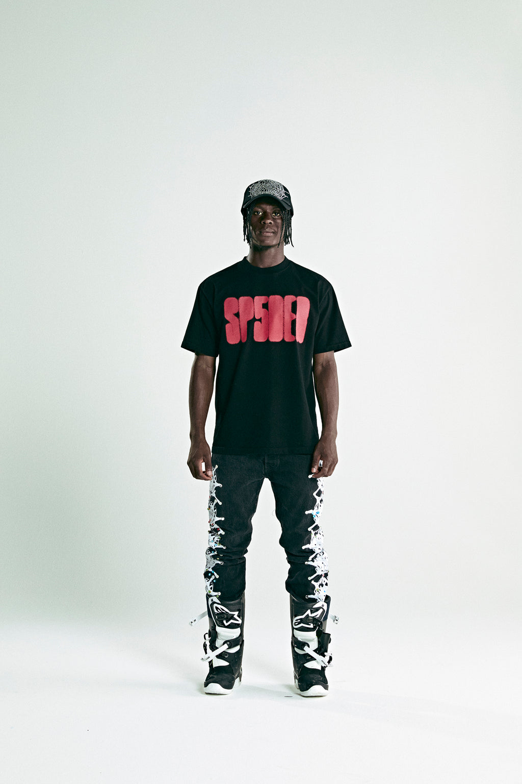 Black cotton FOCUSED LOGO TEE with red 'SP5DER' text print, worn by a man with black jeans and a cap.