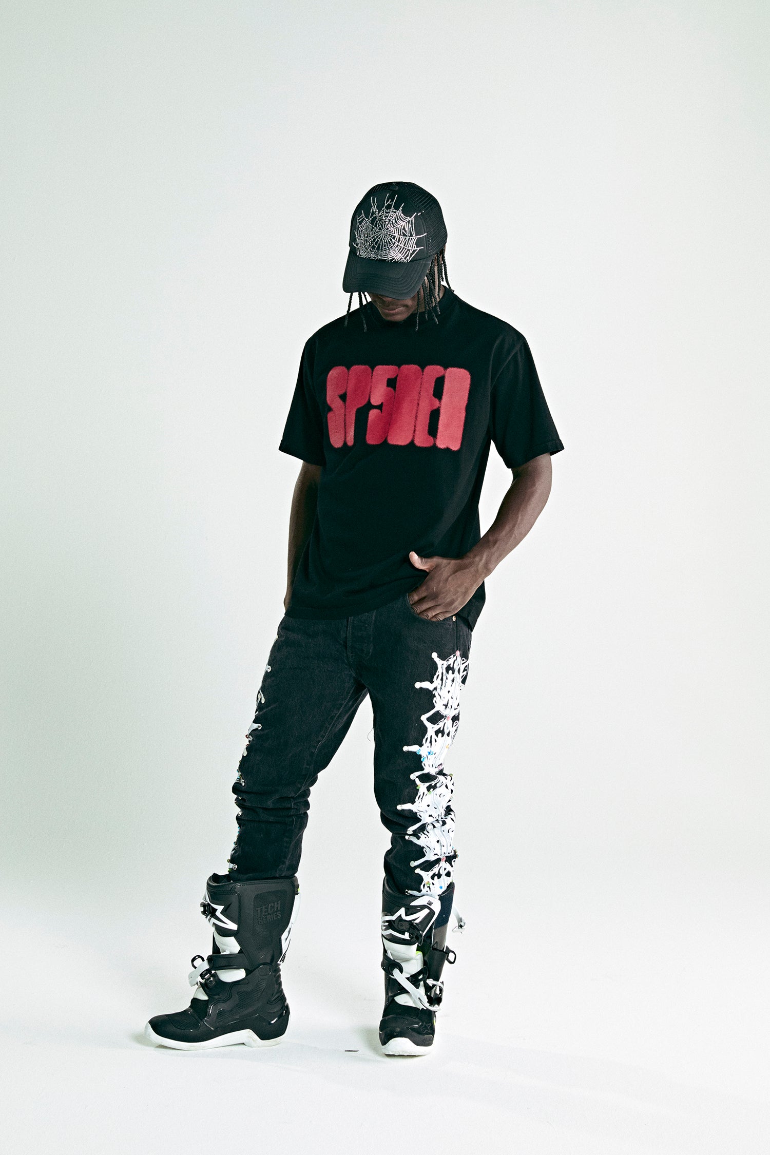 Black cotton tee with red 'SP5DER' text, black jeans with white web design, black boots, and matching cap.