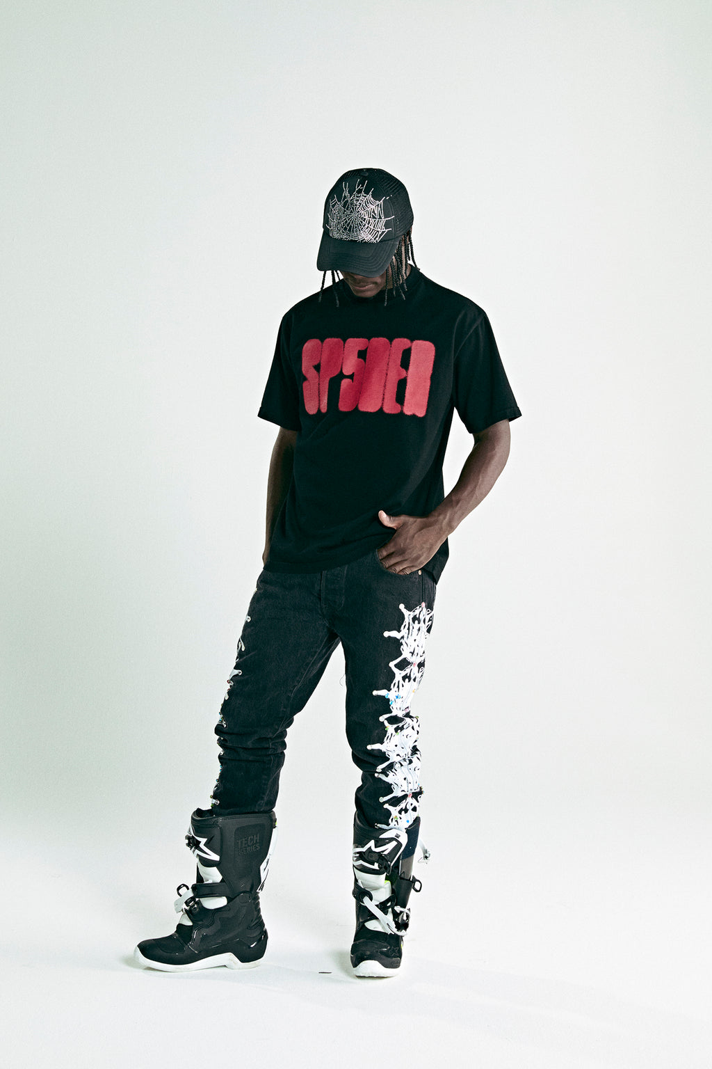 Black cotton tee with red 'SP5DER' text, black jeans with white web design, black boots, and matching cap.