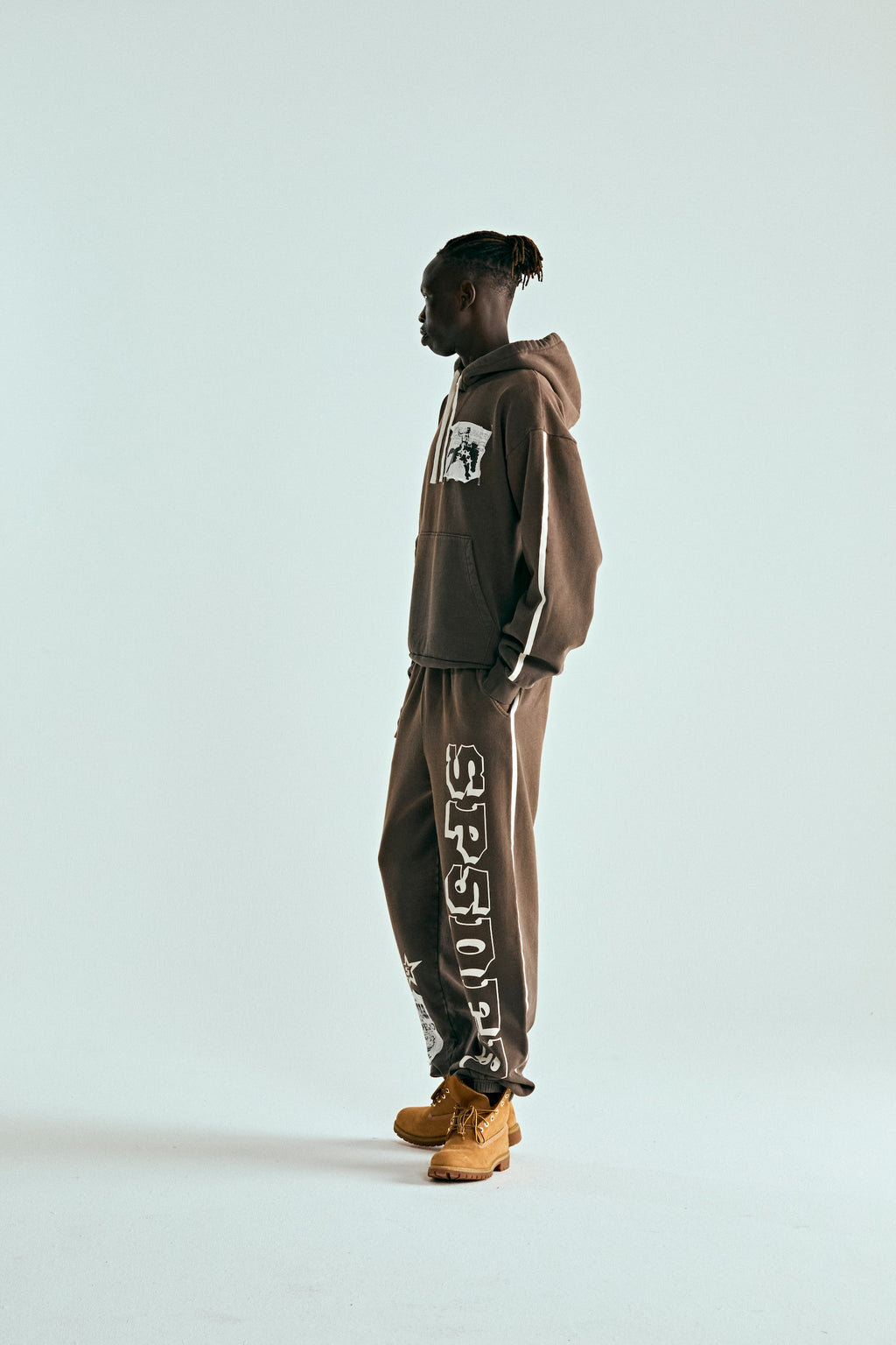 Man in brown 5STAR Rodeo hoodie and matching sweatpants with white stripes and text, wearing tan boots.