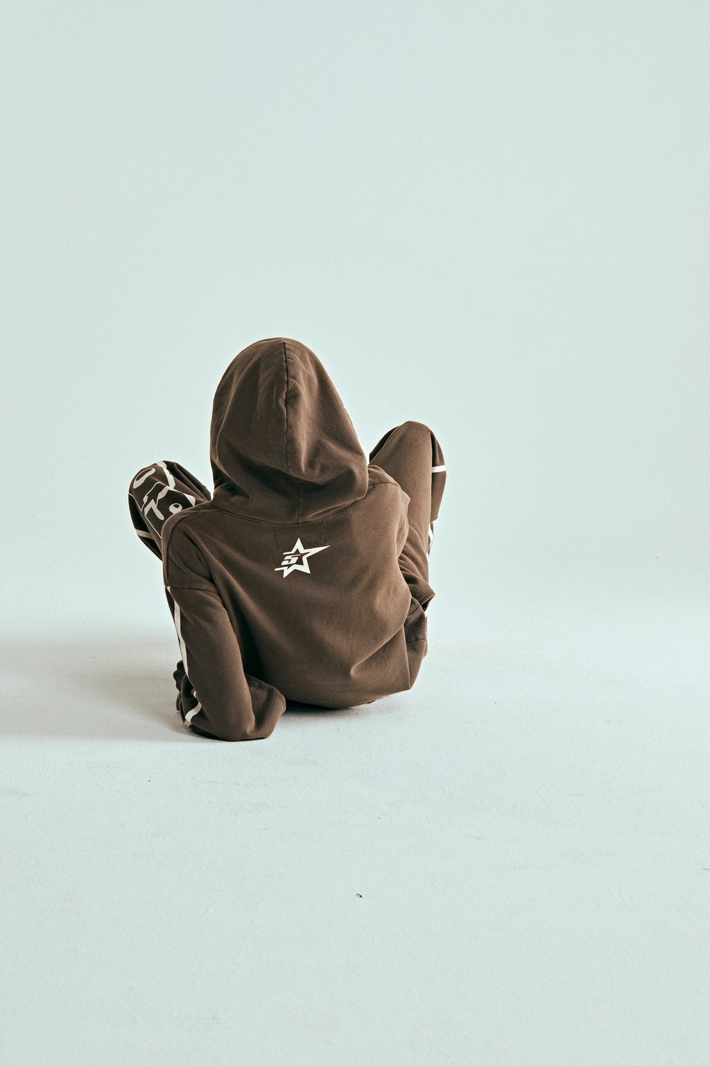 Child in brown 5STAR Rodeo hoodie with white star logo on back, sitting on a light background.