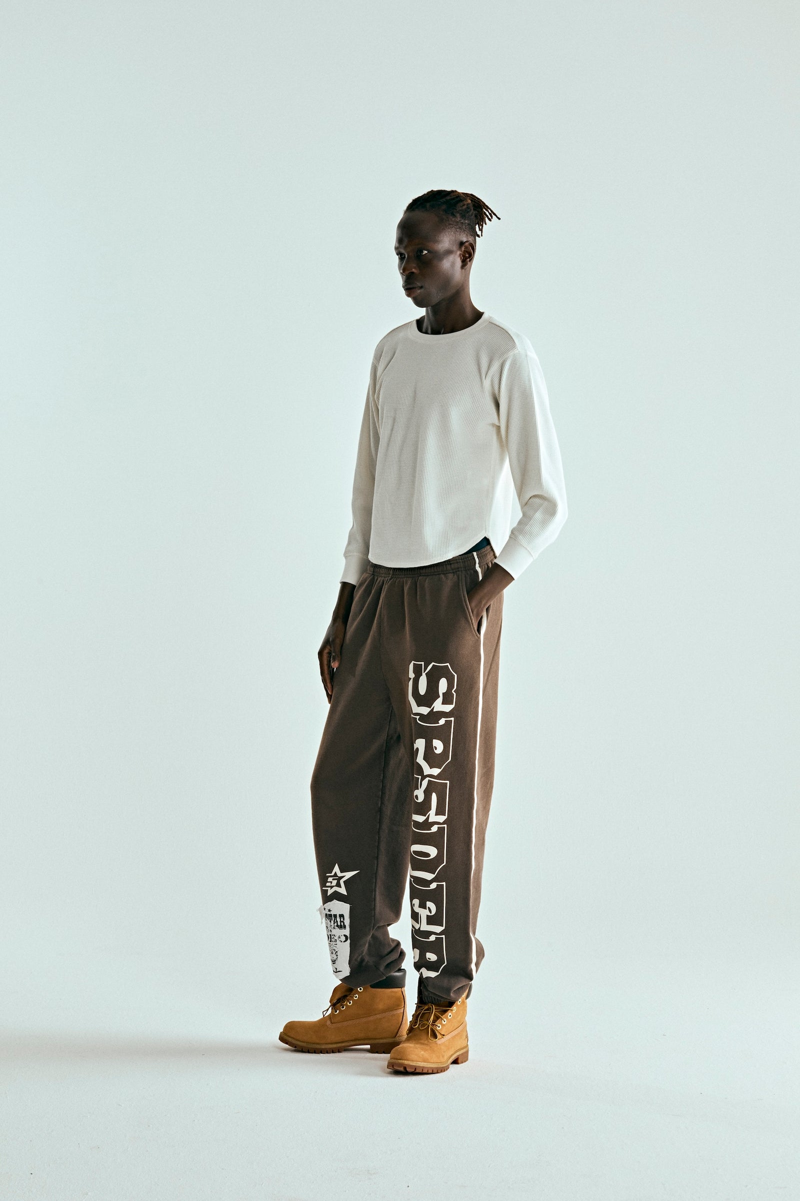 Model wearing brown 5STAR RODEO SWEATPANTS with SP5DER text, side stripe, and distressed patch.