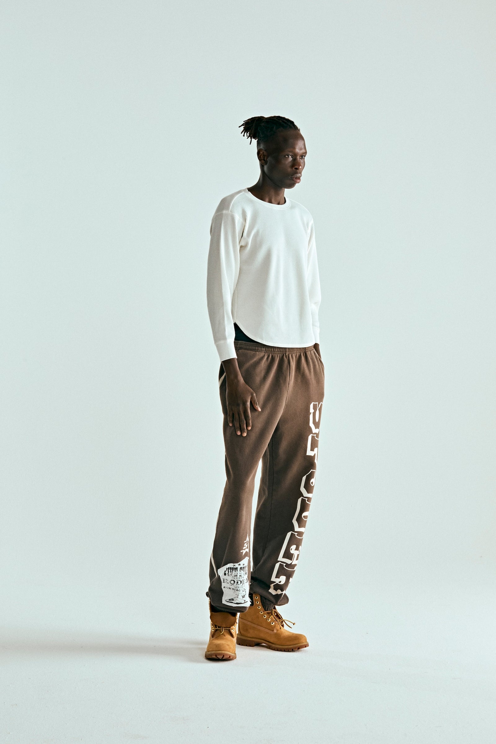 Man in brown 5STAR RODEO SWEATPANTS with white SP5DER text, side stripe, and distressed patch.