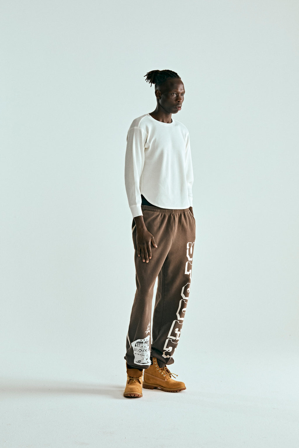 Man in brown 5STAR RODEO SWEATPANTS with white SP5DER text, side stripe, and distressed patch.