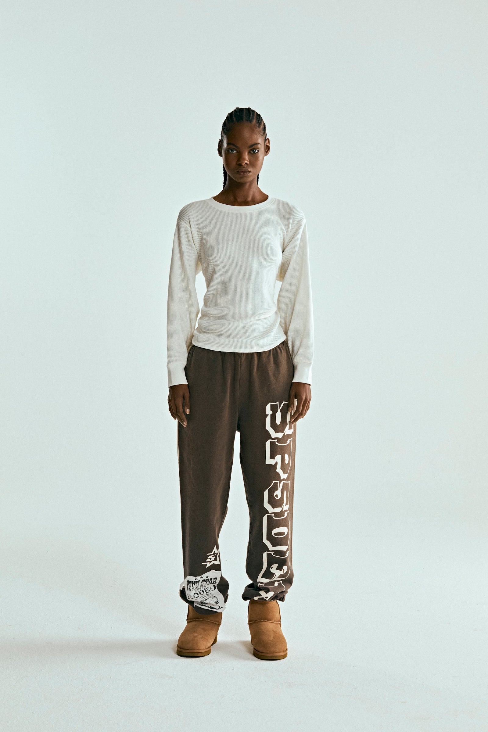 Woman wearing brown 5STAR RODEO SWEATPANTS with SP5DER print, side stripe, and distressed patch.