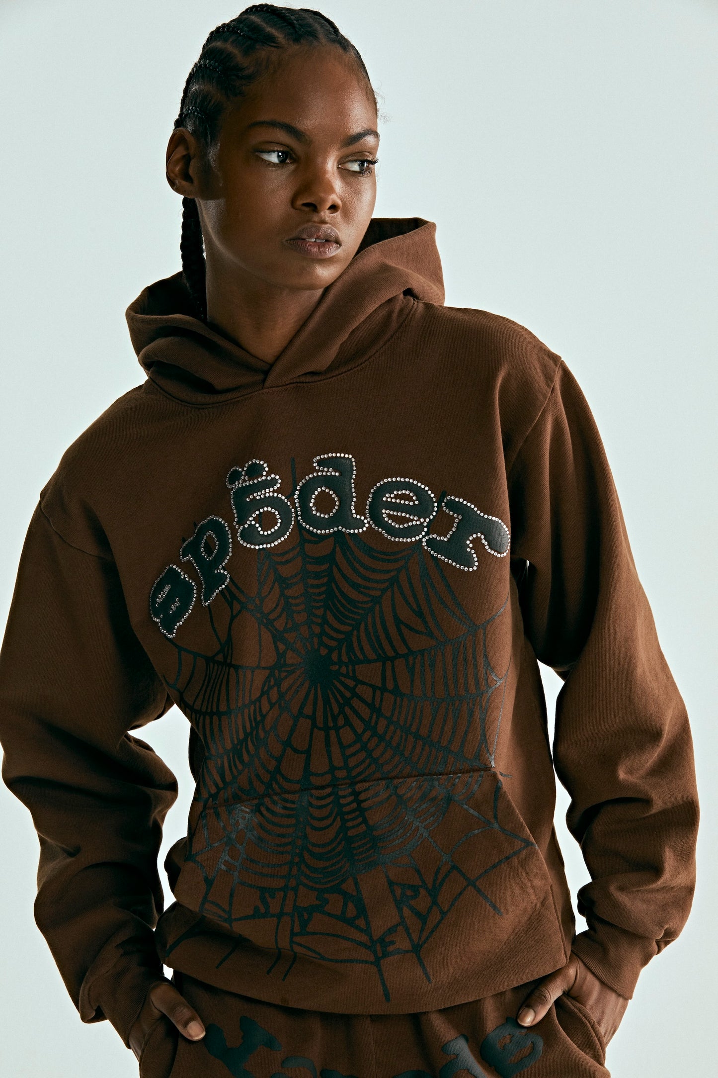 Brown OG WEB HOODIE with rhinestone "SP5DER" text and black spiderweb print, worn by a model.