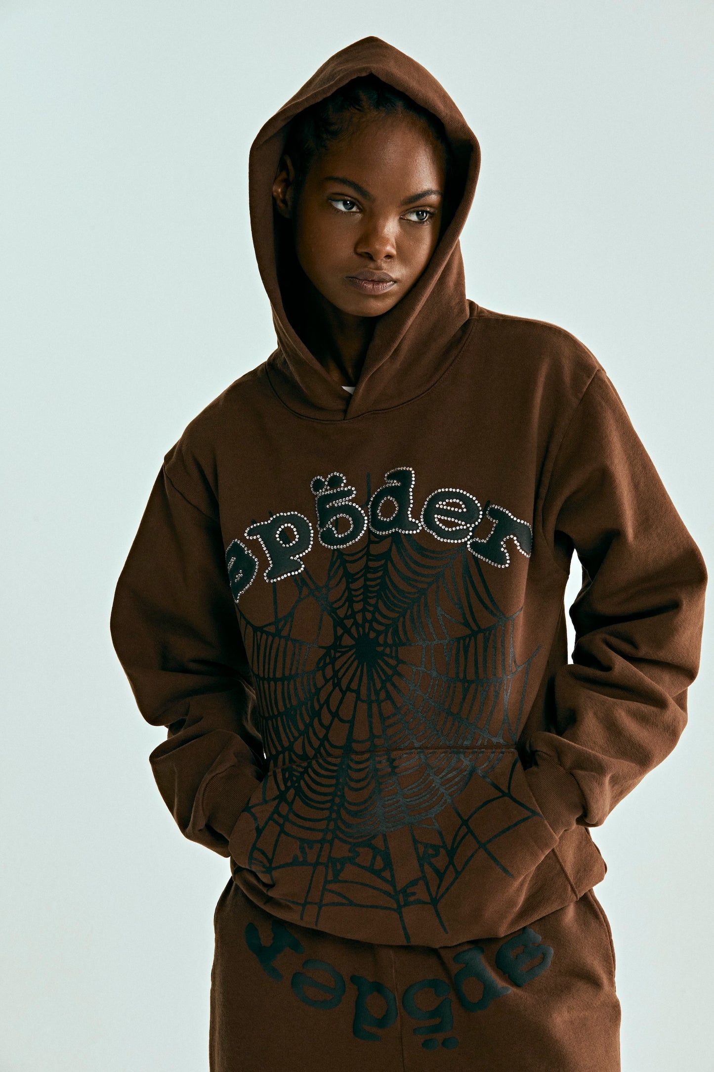 Brown OG WEB HOODIE with rhinestone "SP5DER" text and black spiderweb print, worn by a model.