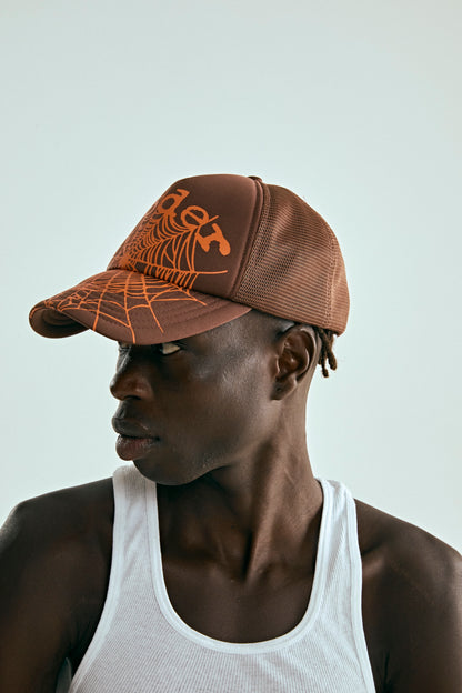 Brown OG WEB V2 trucker hat with orange spiderweb print, curved brim, and mesh back.