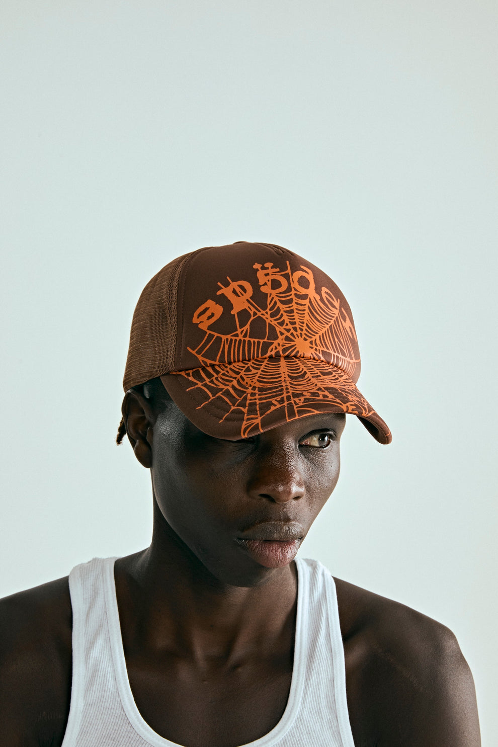 Brown OG WEB V2 trucker hat with orange spiderweb print, curved brim, and mesh back.