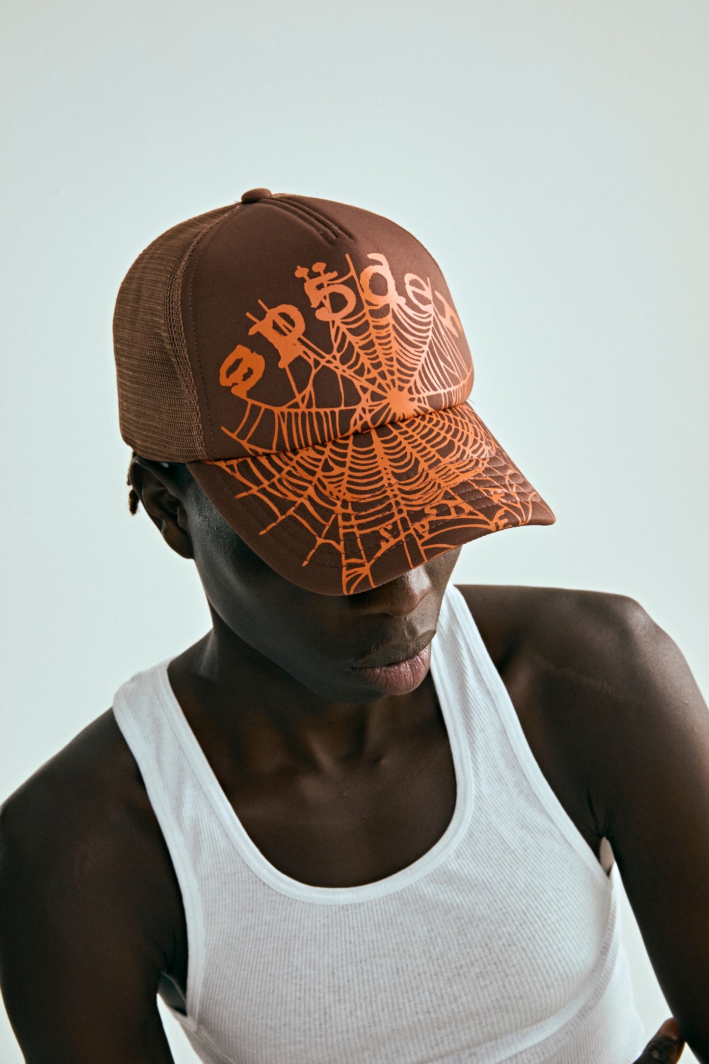 Brown OG WEB V2 trucker hat with orange spiderweb print, curved brim, and mesh back.