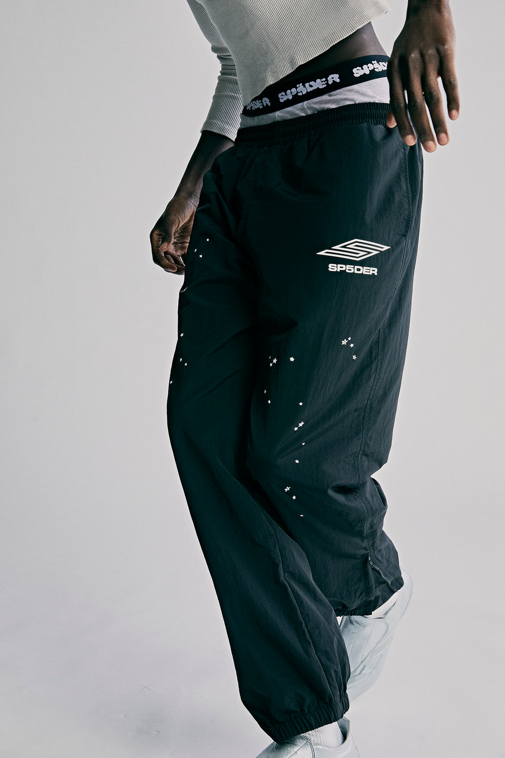 Black nylon ripstop SP5DER PRO wind pants with white logo, scattered stars, and zip cuffs.