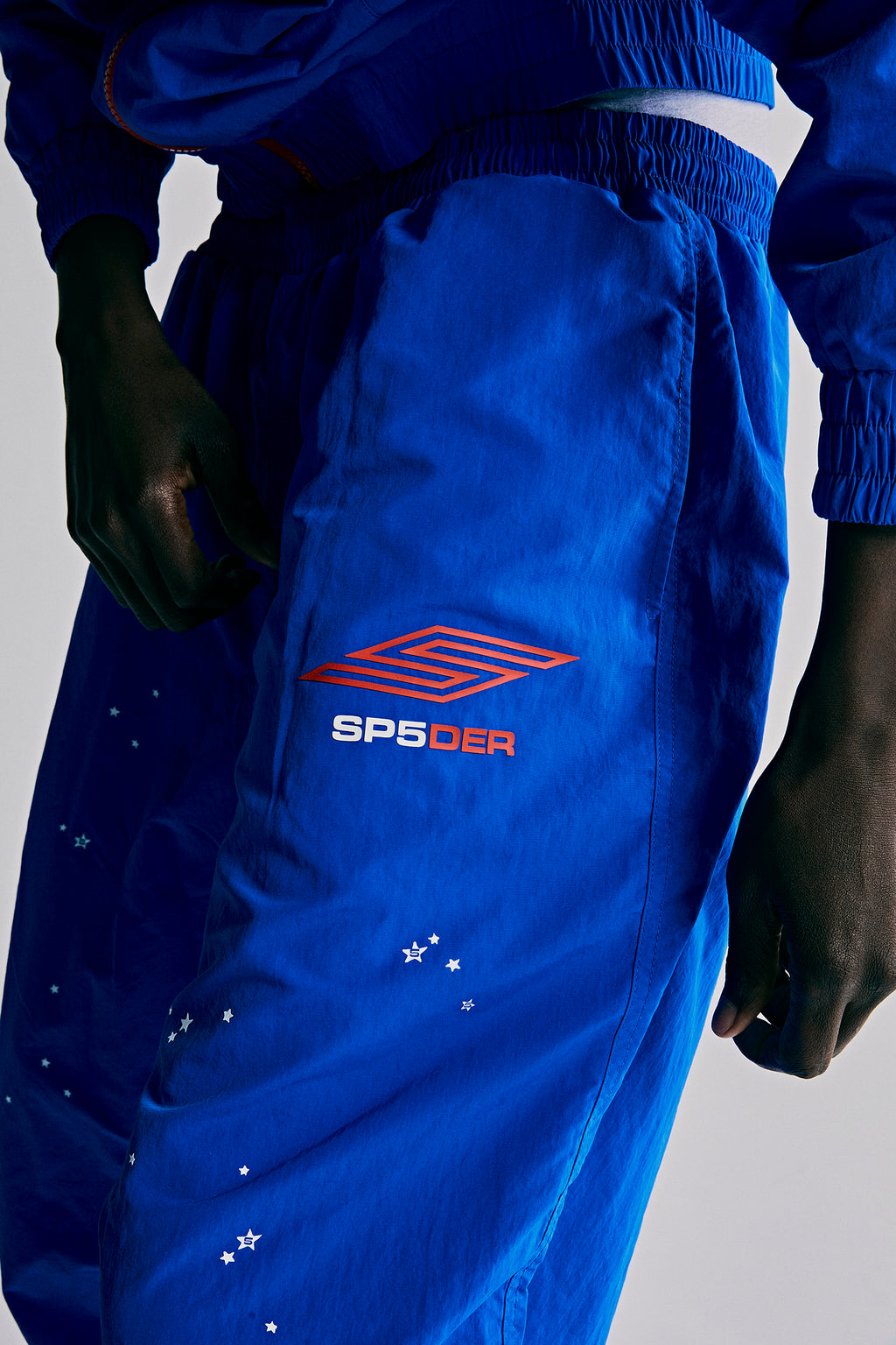 SP5DER PRO royal blue nylon ripstop wind pants with orange logo and white star print.