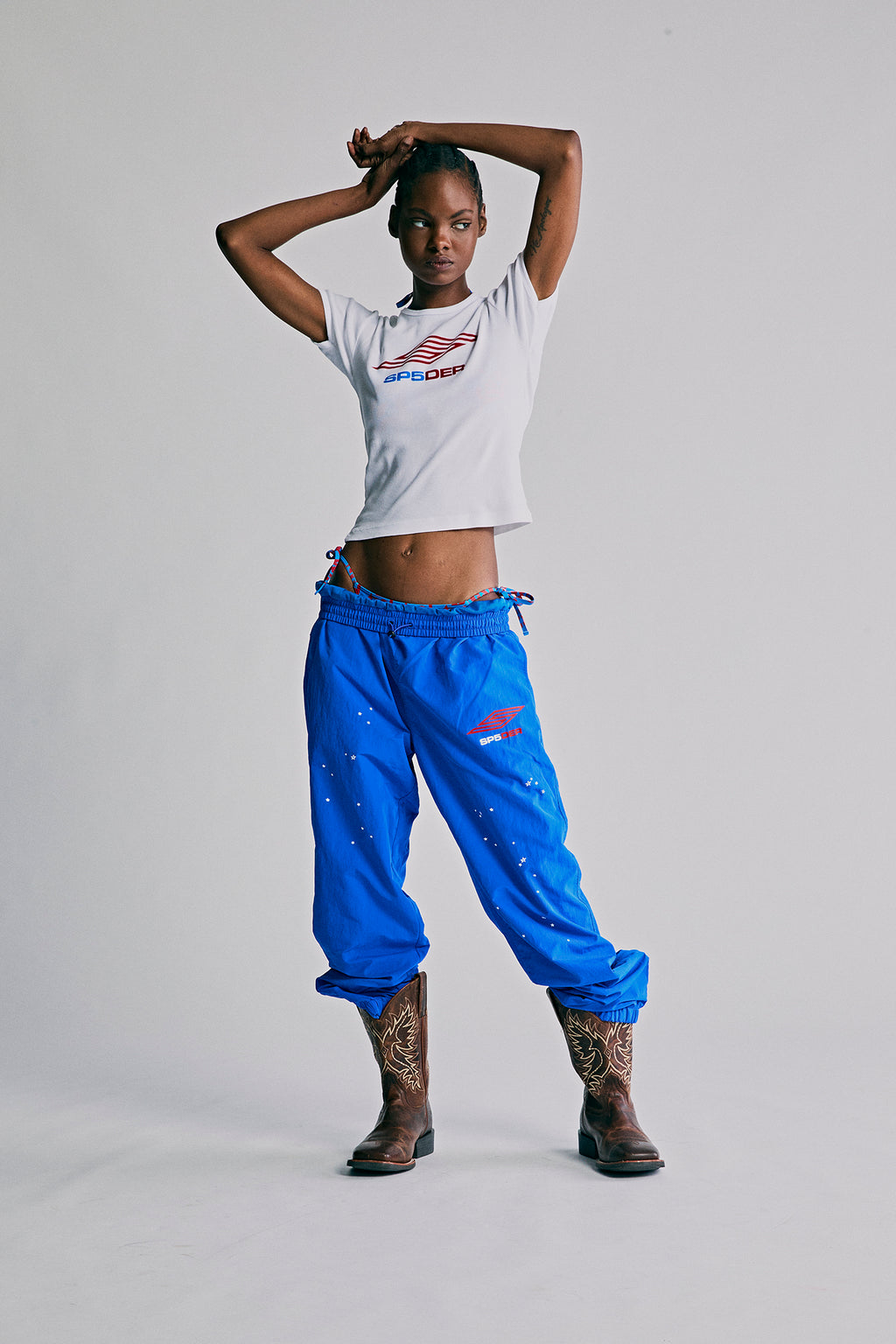 Model wearing blue SP5DER PRO WIND PANTS with scattered star print, SP5 Pro logo, and zip cuffs.