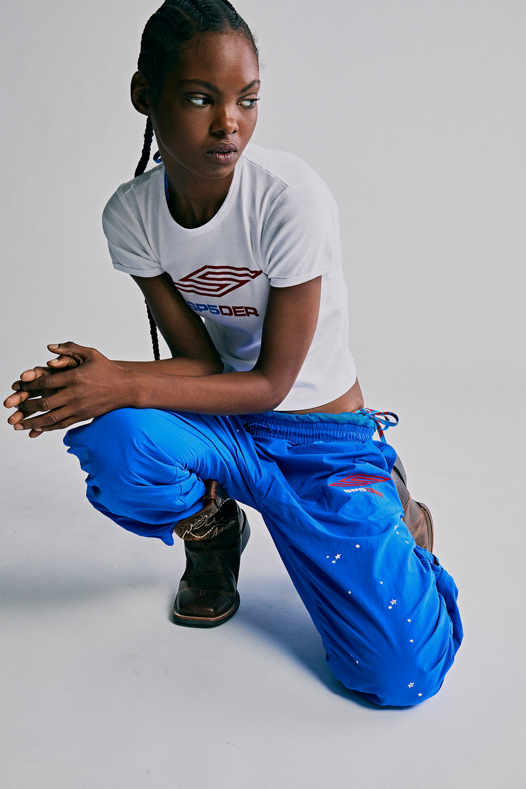 Model wearing SP5DER PRO blue nylon ripstop wind pants with star print and logo, paired with a white tee.