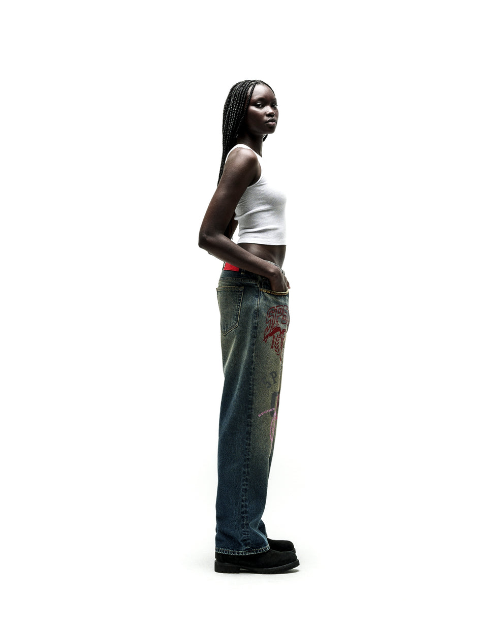 Woman in baggy blue jeans with red and pink graphic prints, white tank top, and black shoes.