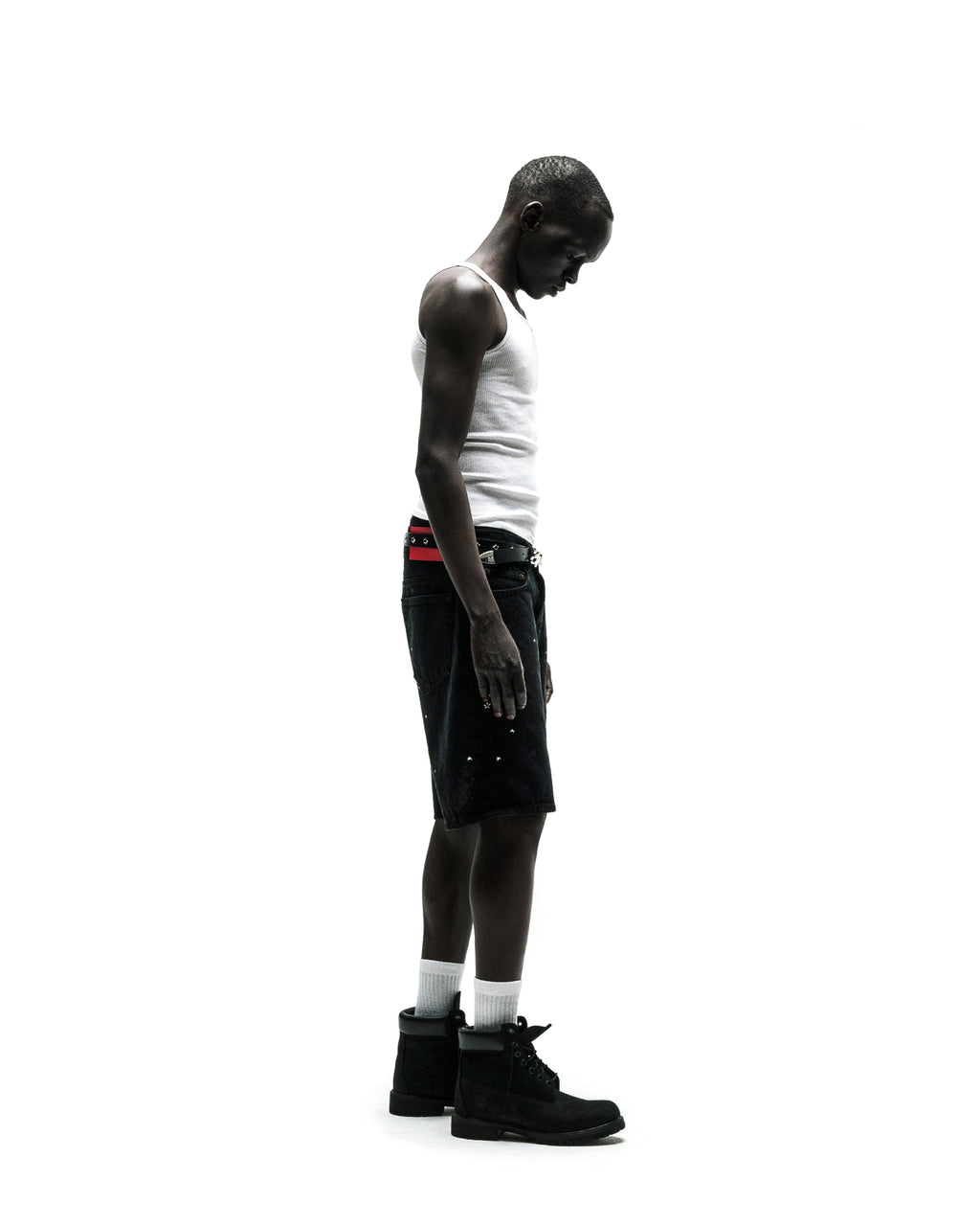 Man in black denim jean shorts, white tank top, red belt, and black boots.