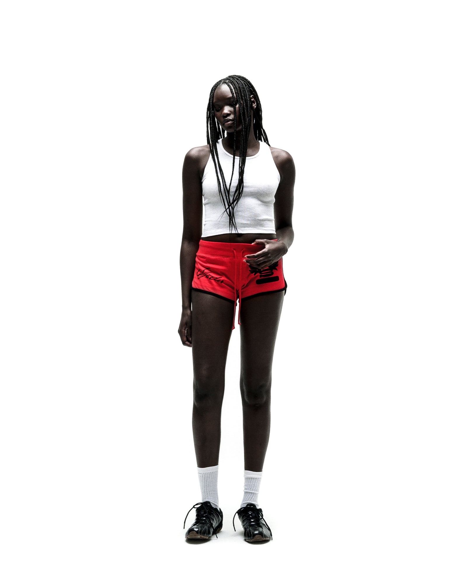 Woman in red SP5 WIDE BOXER shorts with black trim, white crop top, and black sneakers.