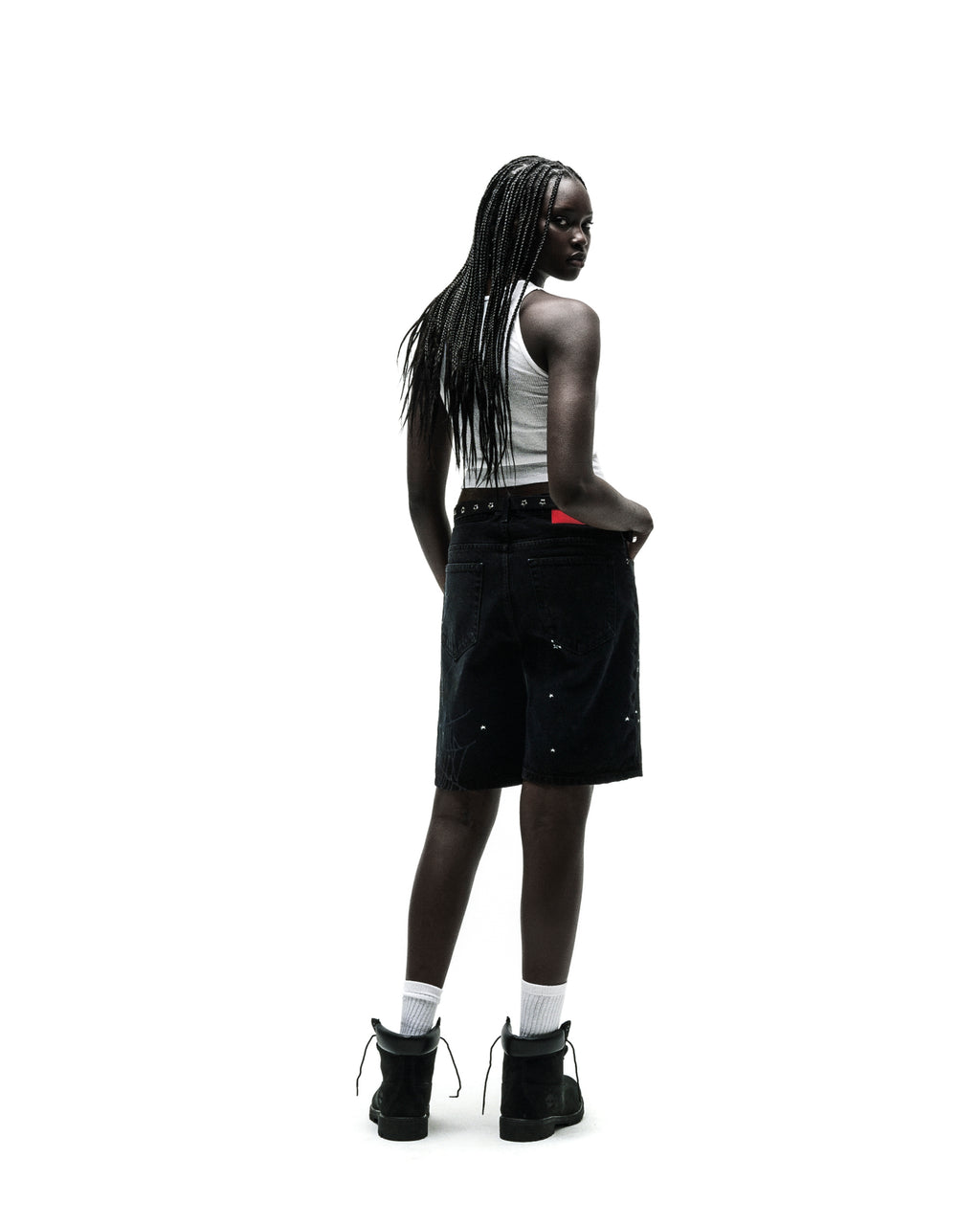 Woman in black HEAVY WEB JEAN SHORTS with white paint splatters, a white tank top, and black boots.