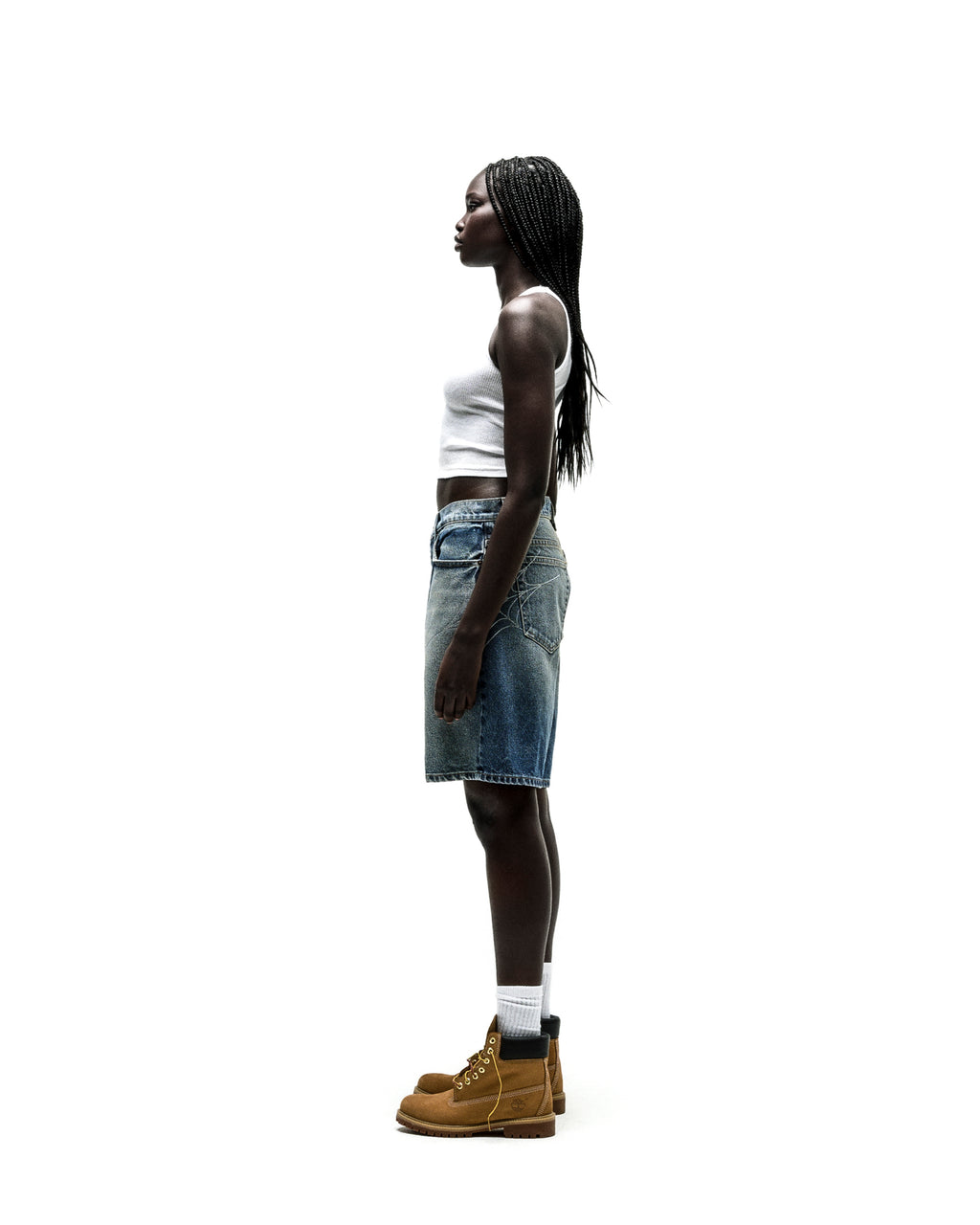 Woman in vintage wash denim shorts with rhinestone web design, white crop top, and brown boots.
