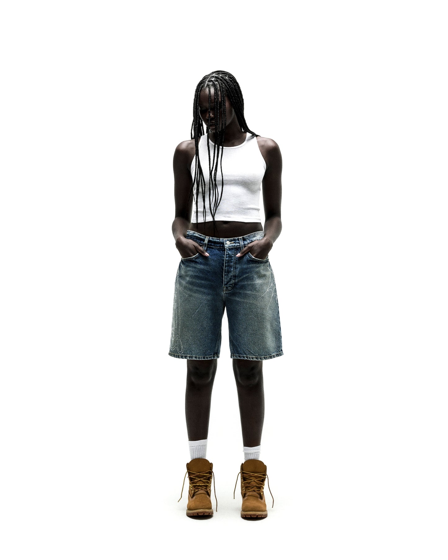 Model in vintage wash denim shorts with rhinestone web design, white tank top, and brown boots.