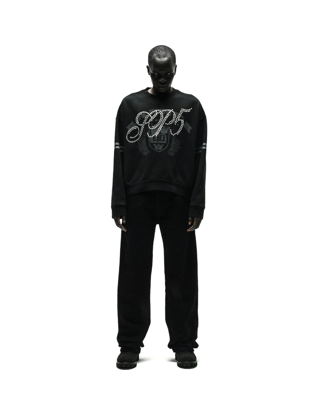 Black ARANEA CREWNECK with "SP5" rhinestone logo and striped sleeves, worn by a model.