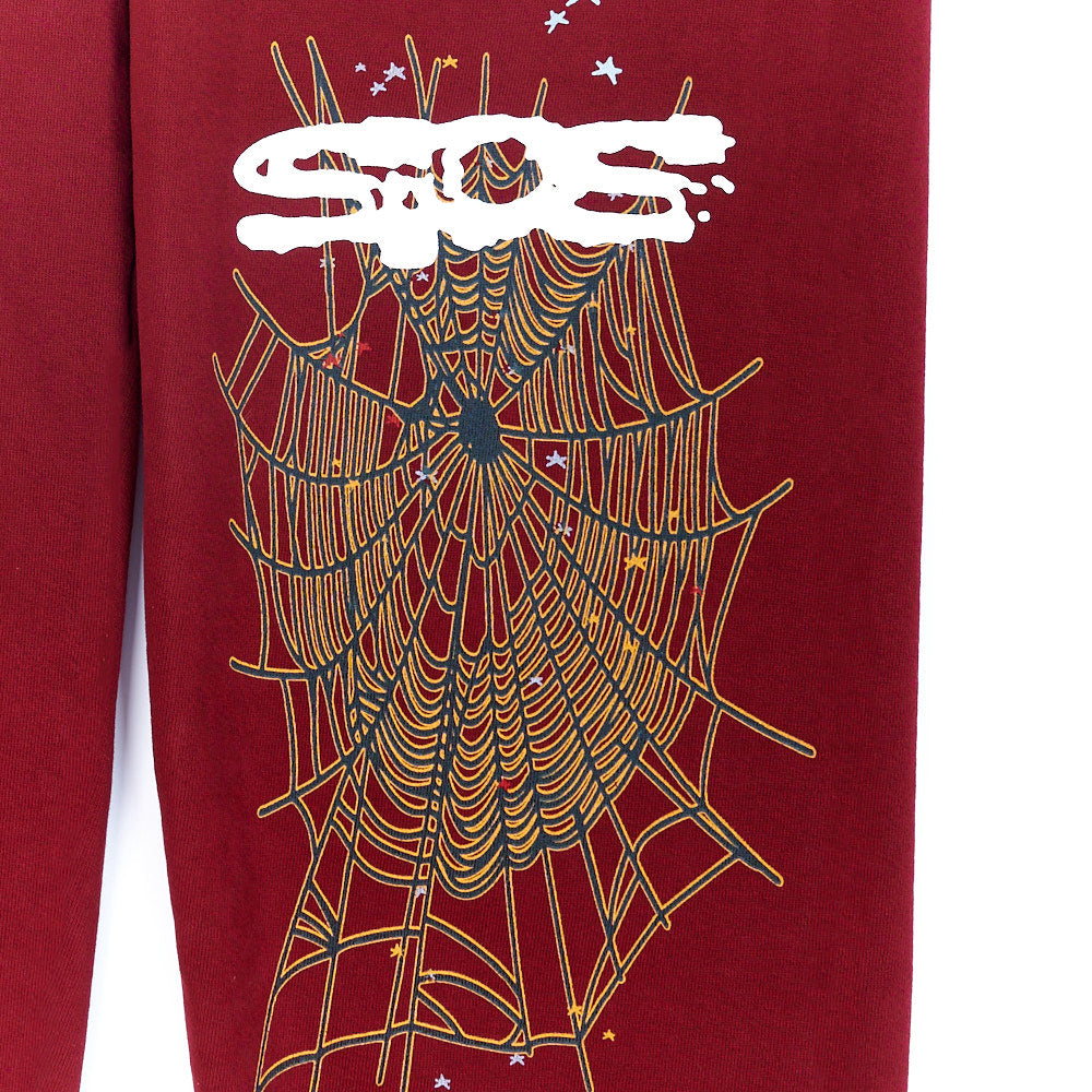 Red SP5DER sweatpant with white puff print logo and detailed gold/black spider web graphic.