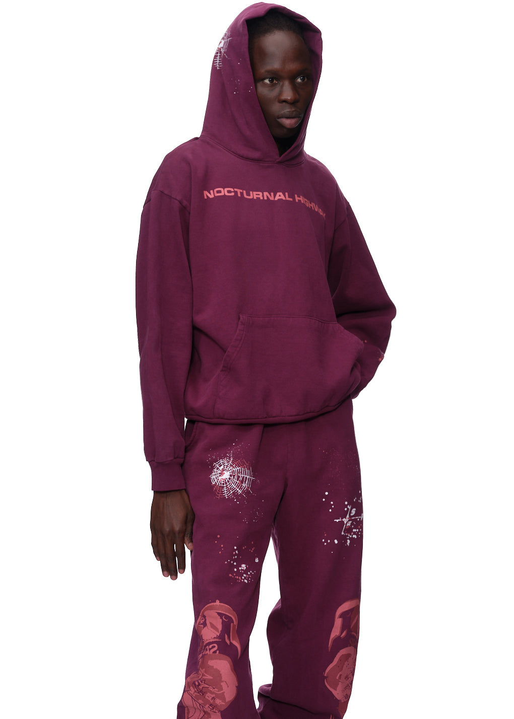 Man in a maroon "Nocturnal Highway" hoodie with puff print and matching sweatpants with white paint splatters.