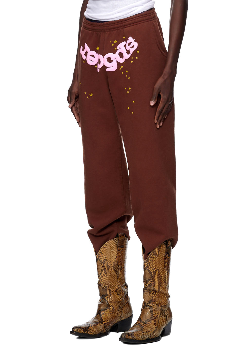 Brown CLASSIC SWEATPANT with pink puff print "Sp5der" logo and gold stars, worn with snakeskin boots.