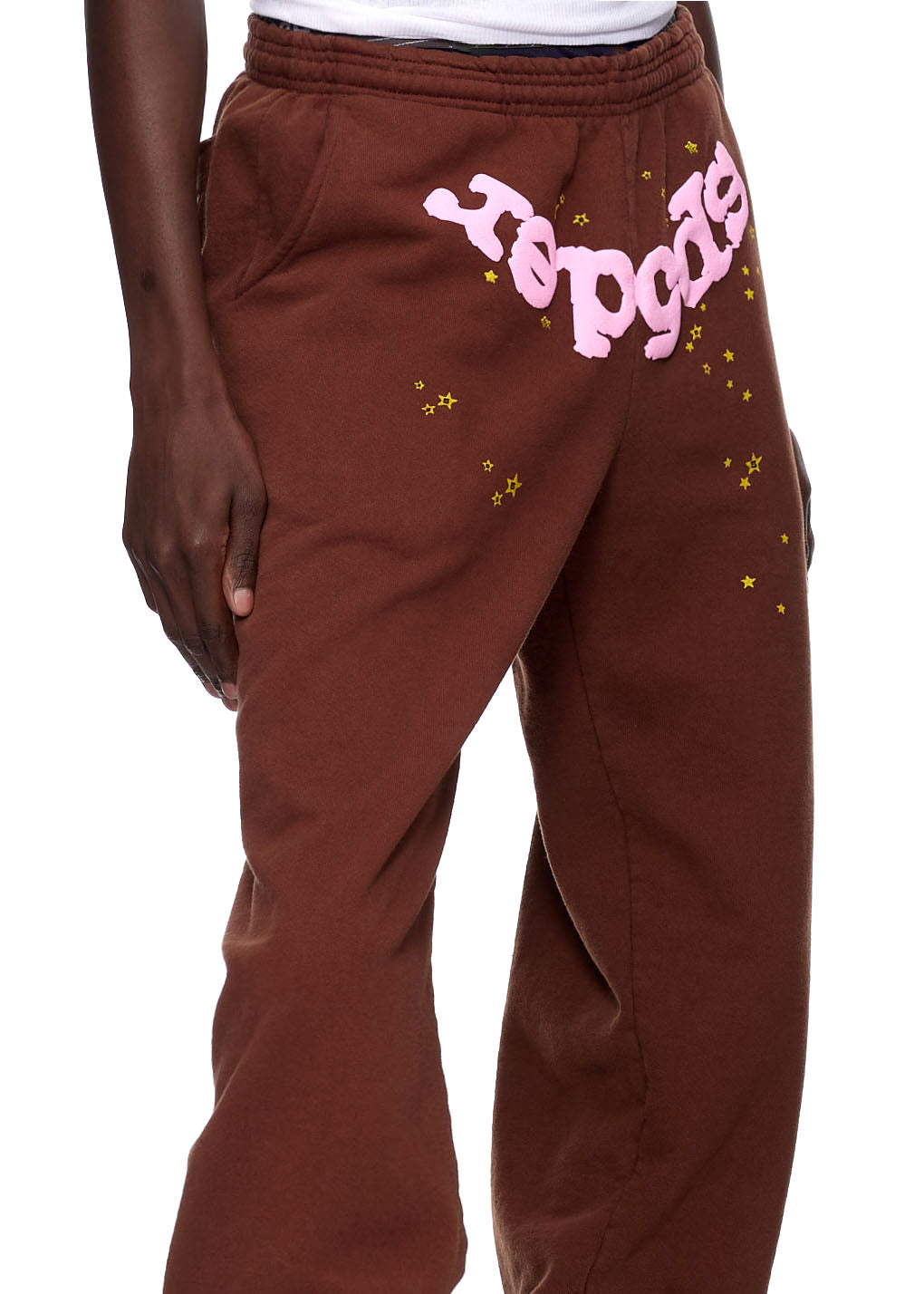 Brown fleece sweatpants with pink puff print "SP5DER" logo and yellow star details.