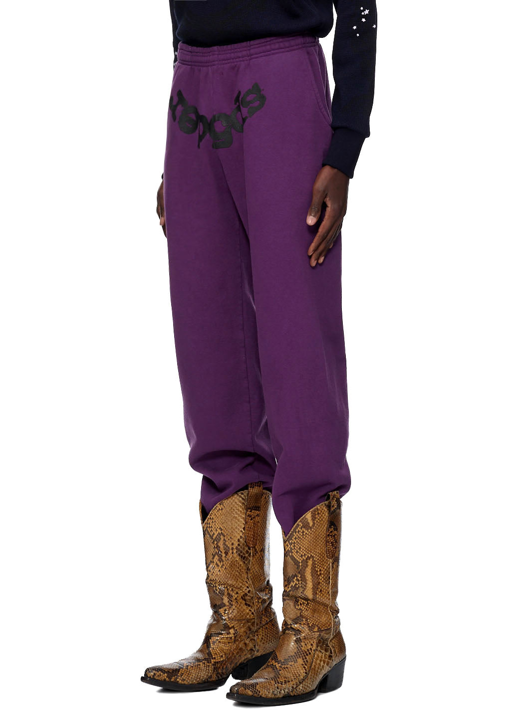 Purple CLASSIC SWEATPANT with black puff print and SP5DER web print, worn with snakeskin boots.