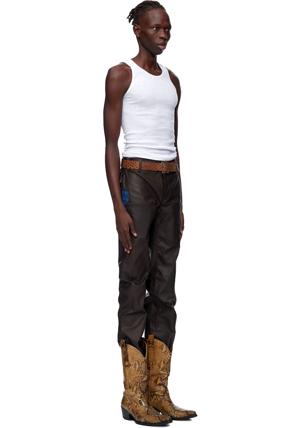 Model wearing brown coated canvas SP5DER front pocket jeans with branded tack buttons and high-density embroidery.
