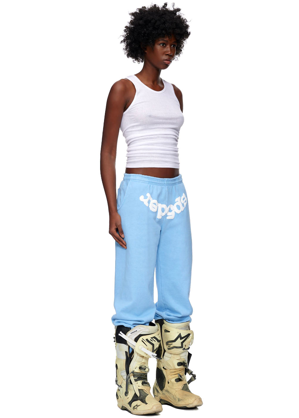 Model wearing light blue CLASSIC SWEATPANTS with white "sp5der" puff print and web design, paired with a white tank top.